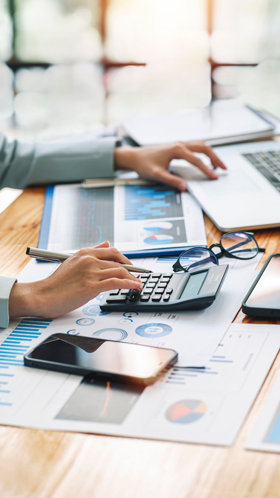 Hands using a calculator beside a laptop and financial reports