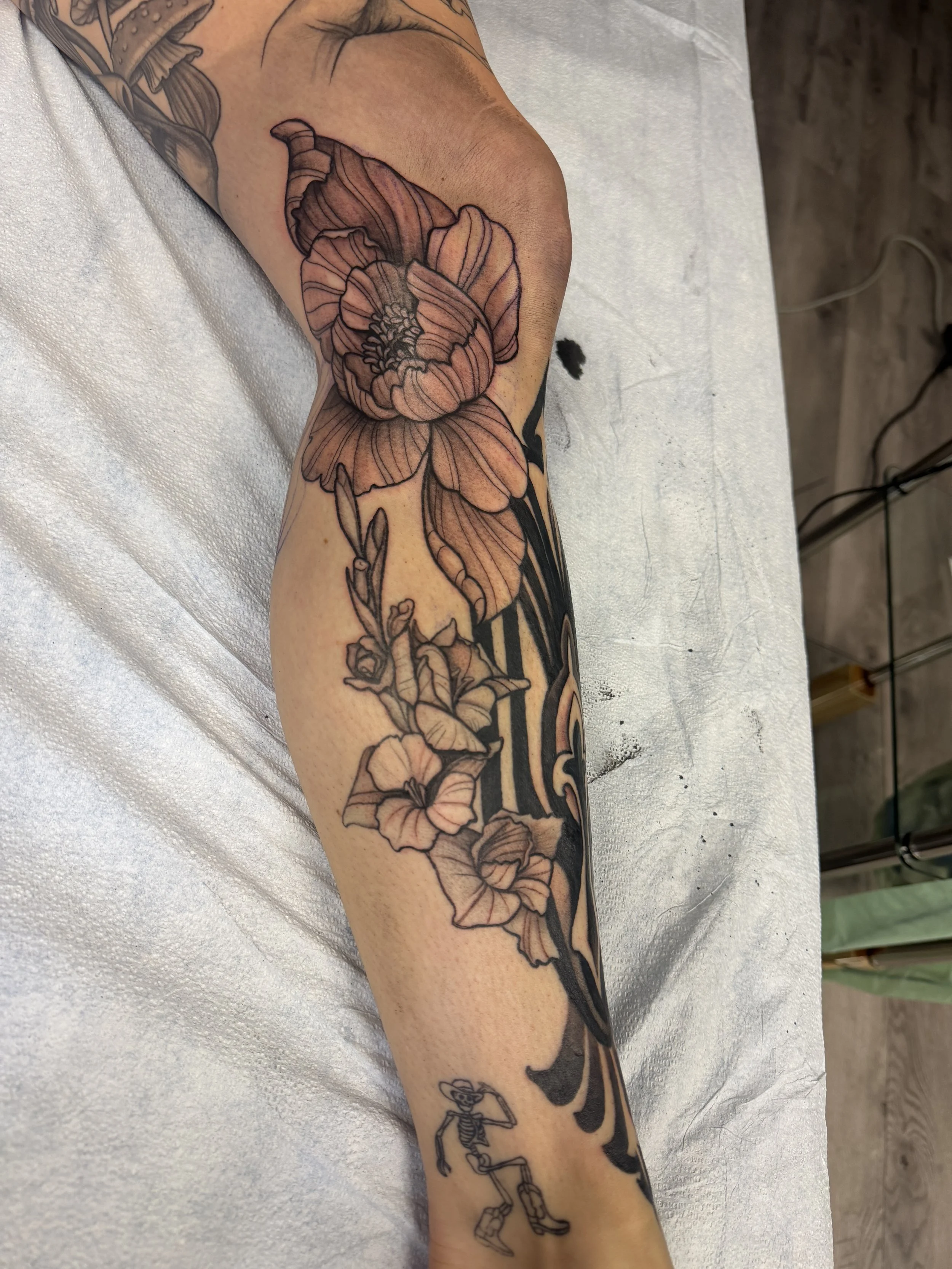 A tattoo on a person's arm featuring a large, detailed flower, with additional tattoo elements including a skeleton figure.