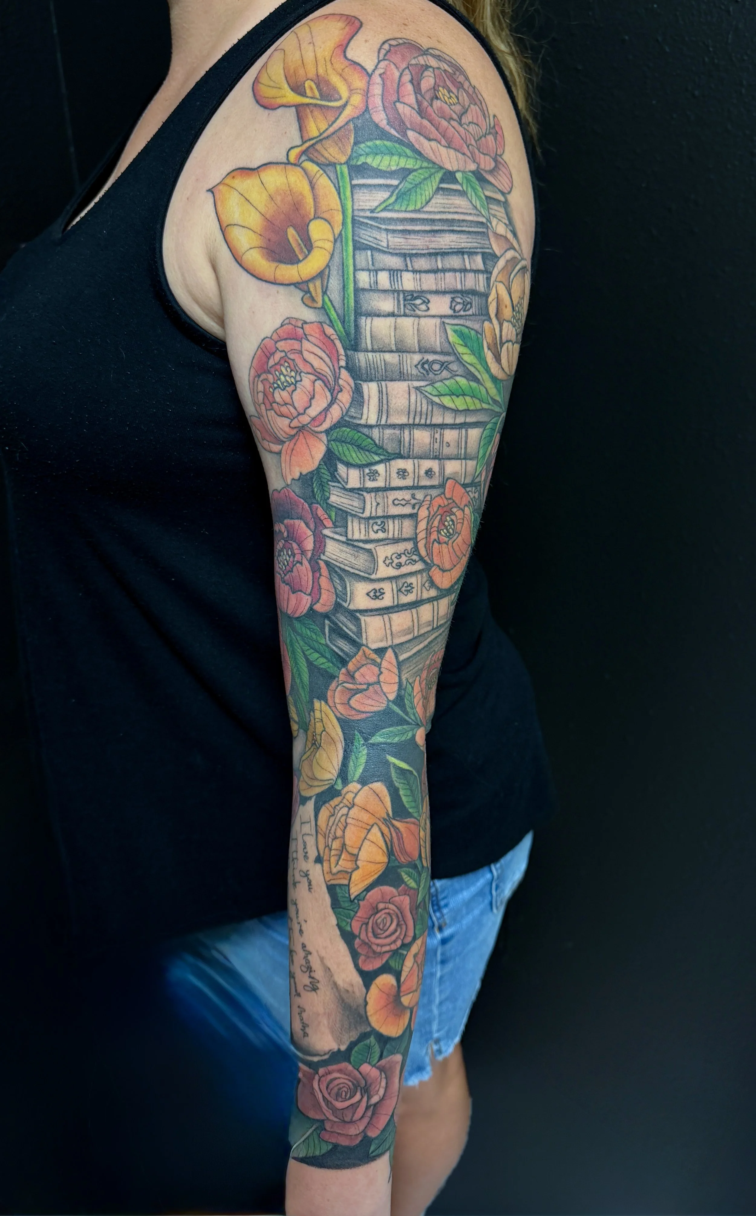 Colorful sleeve tattoo featuring roses, a bookshelf with detailed spines, and various leaves.