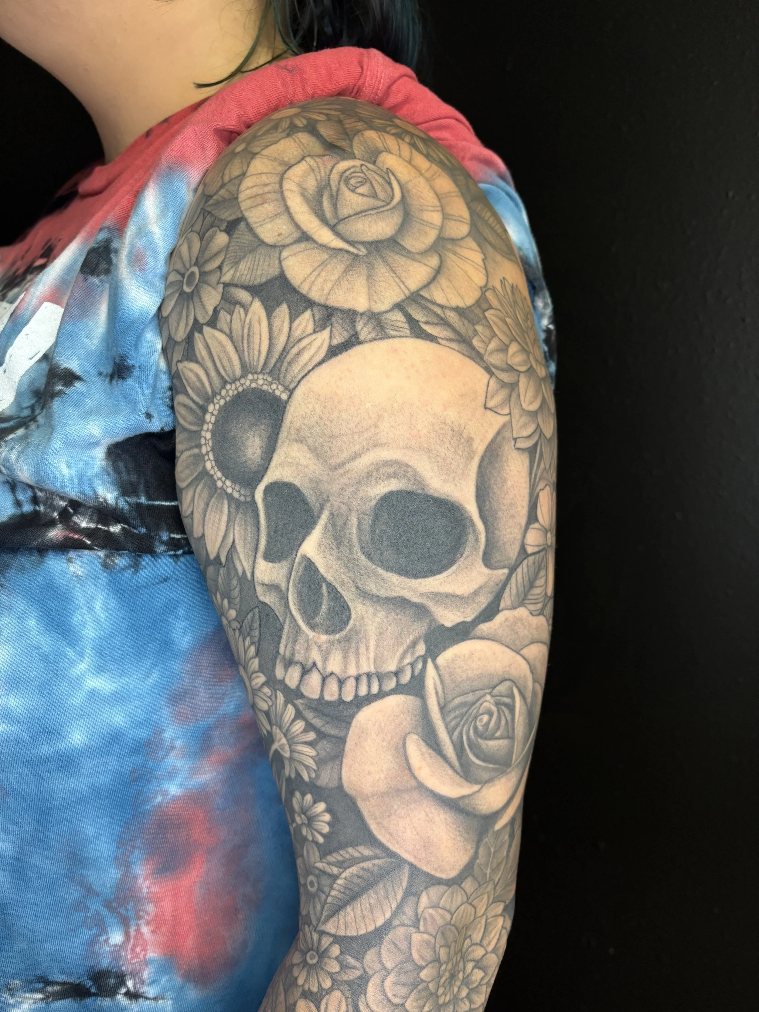 Tattoo of a skull surrounded by flowers on a person's arm.