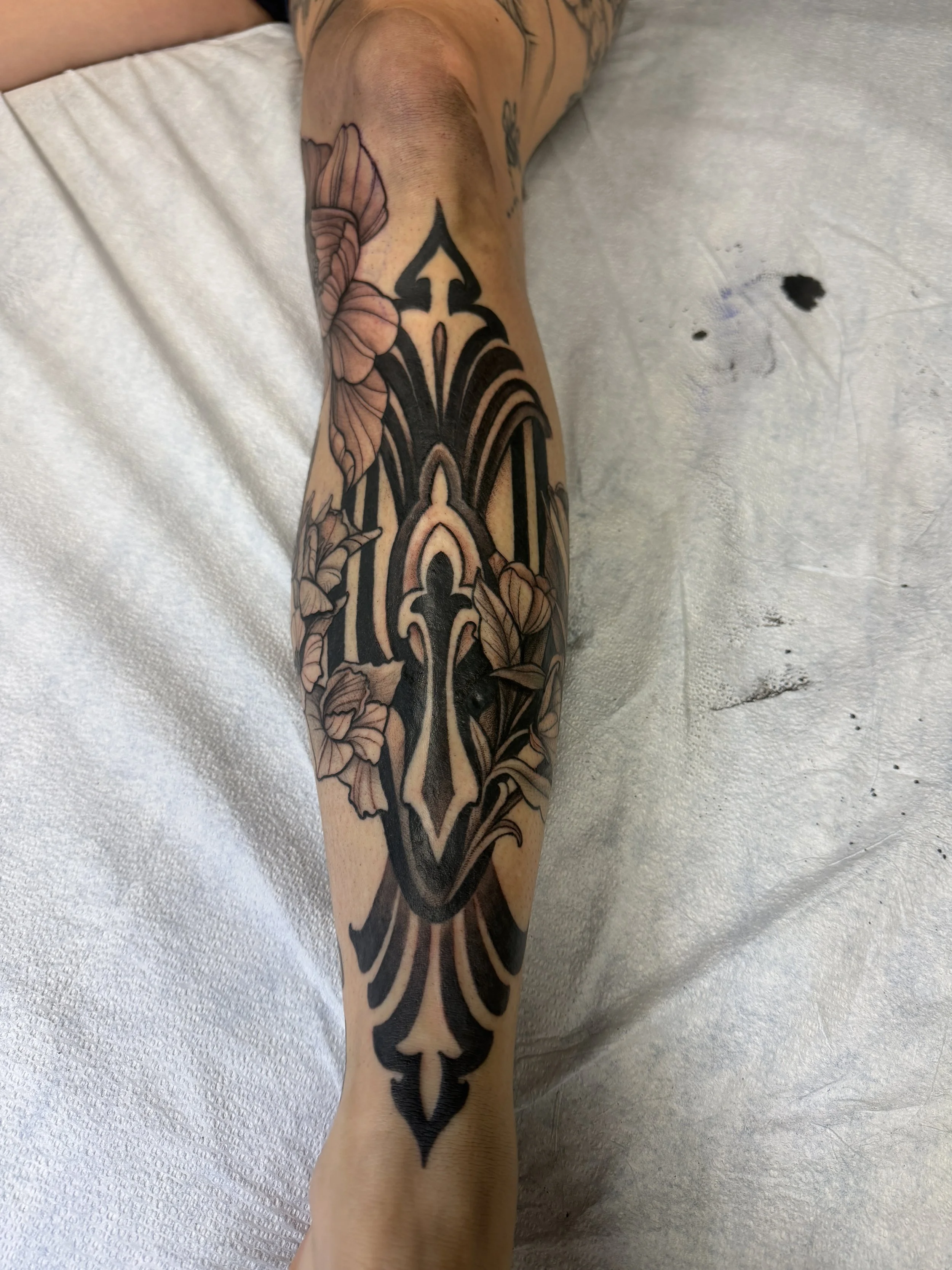 A tattoo on a person's arm featuring a large, black and gray Gothic-style design with floral elements.