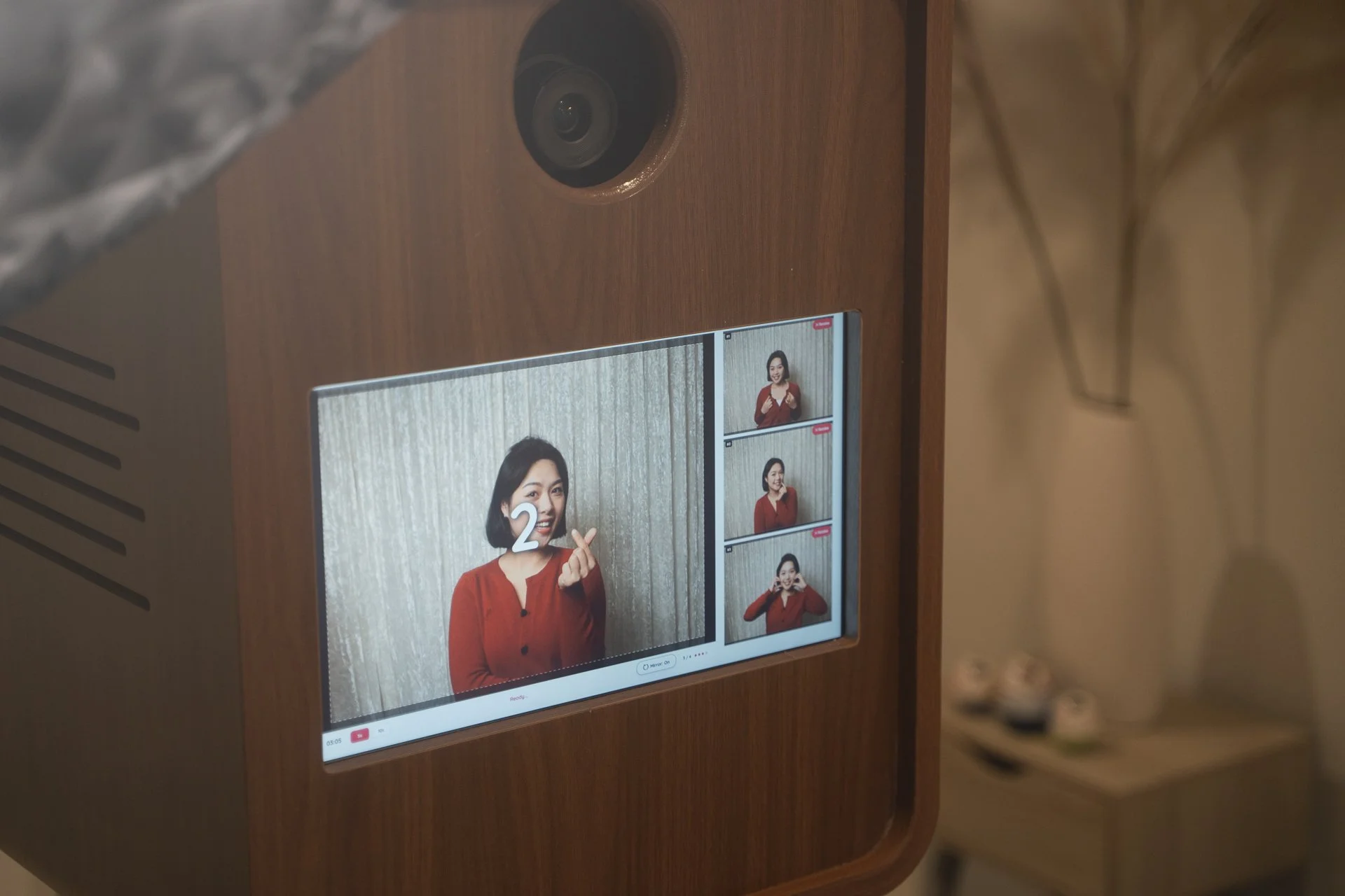 Photo of an intercom or video doorbell system showing a woman in a red top making various gestures, with multiple video call thumbnails on the screen.