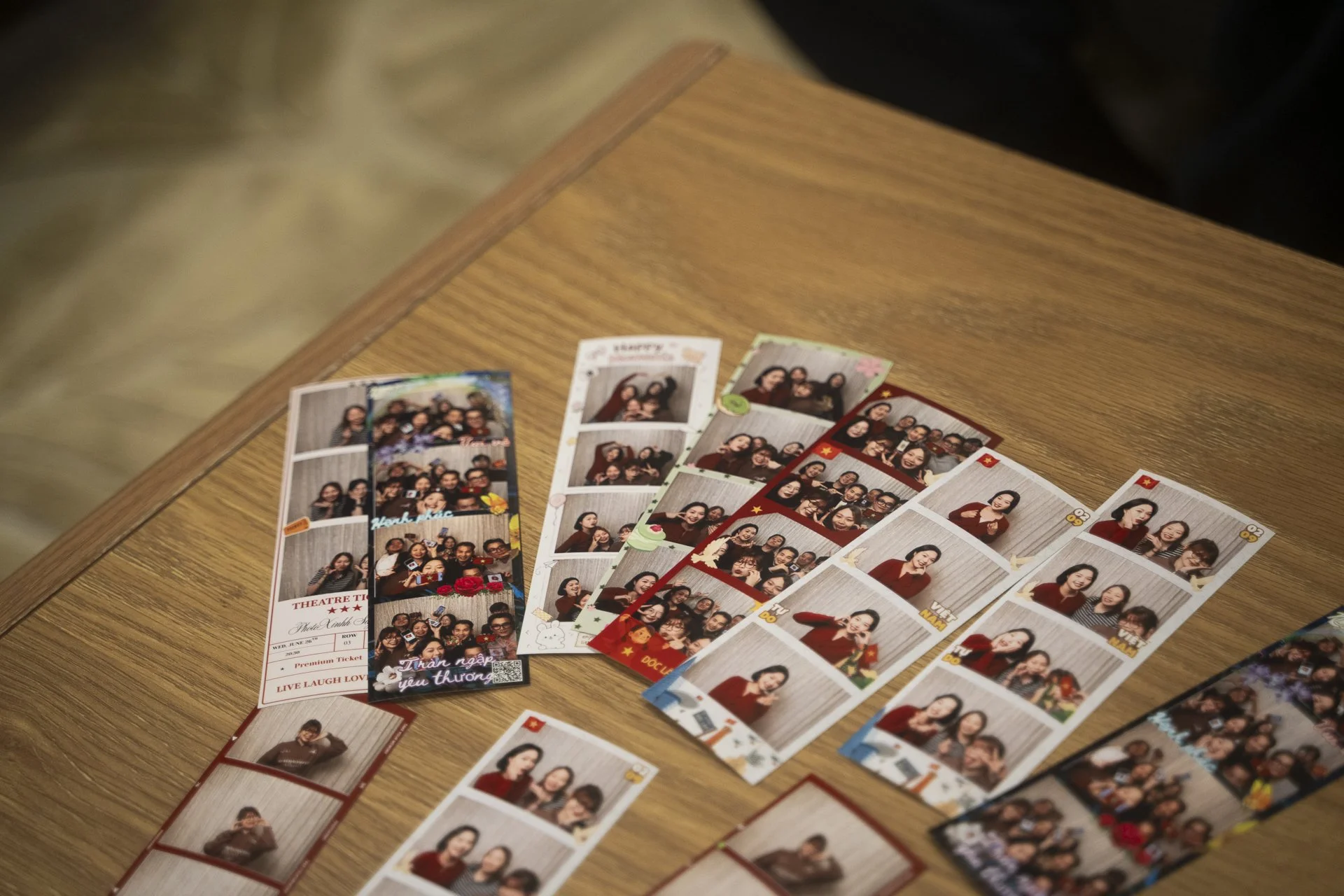 Photo of several photo booth picture strips on a wooden table, featuring groups of people smiling and posing for the camera.
