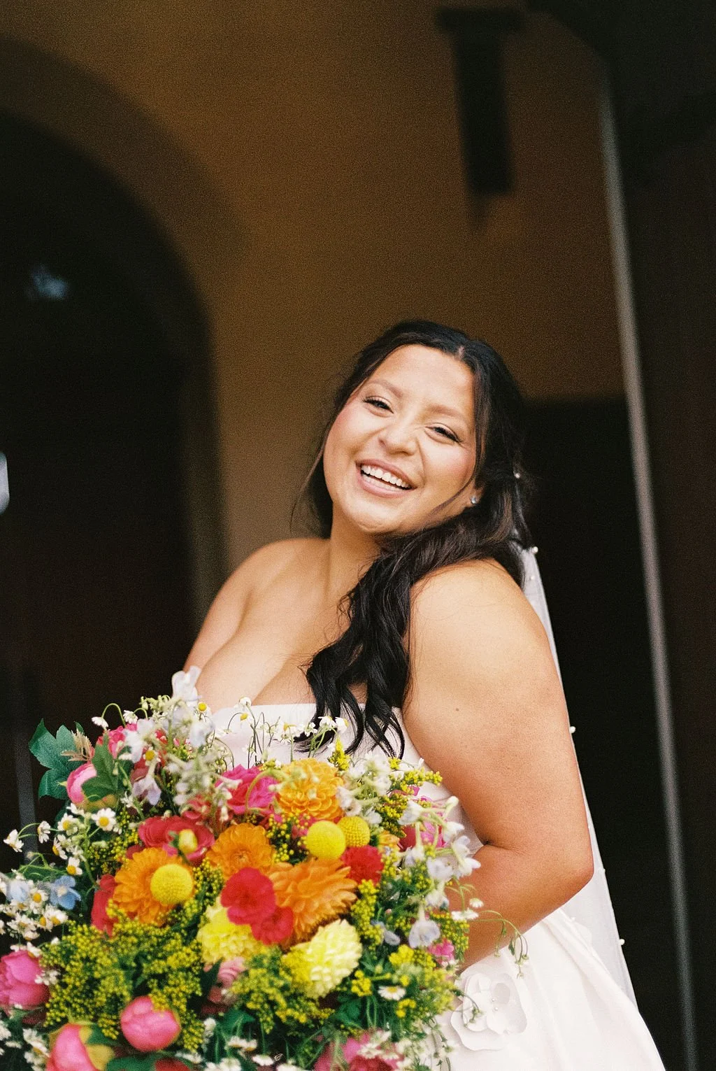 A woman in a white dress holding a colorful bouquet of flowers and smiling happily.