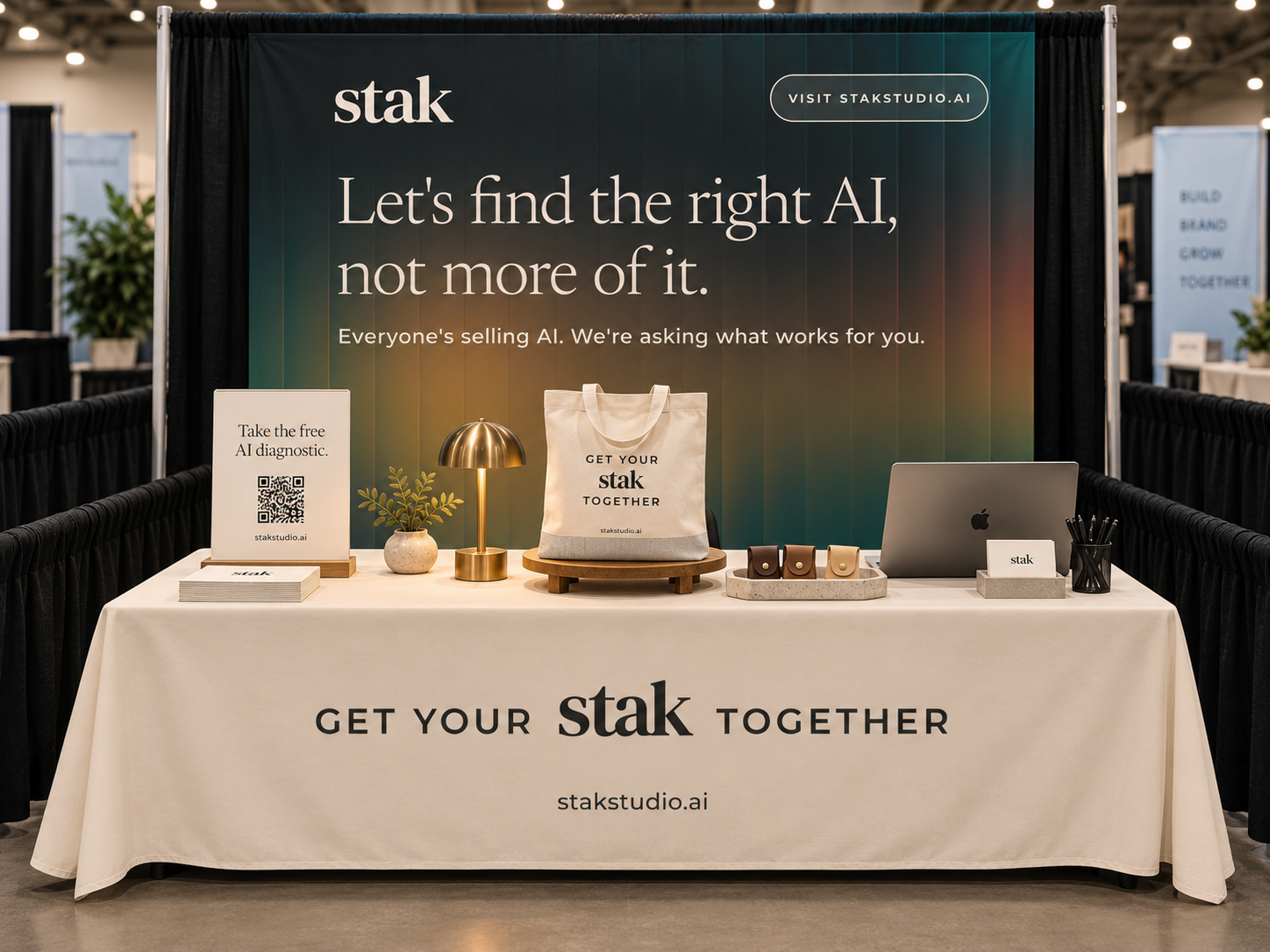 Trade show booth for Stak Studio with a large backdrop displaying the slogan 'Let's find the right AI, not more of it,' and a table with promotional materials, a laptop, a tote bag, small leather items, and a sign with a QR code.