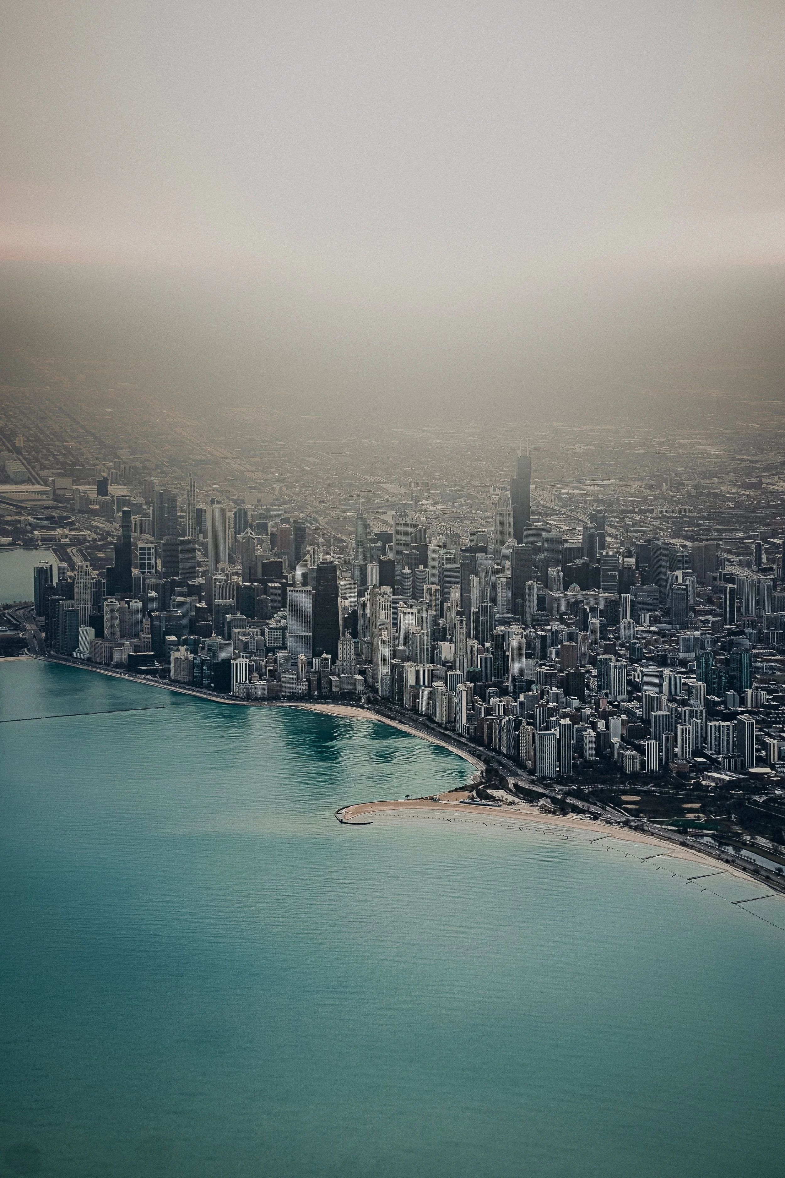 Aerial view of a city with tall skyscrapers along the coastline, including a beach with a sandy shore, and a large body of water in the foreground.