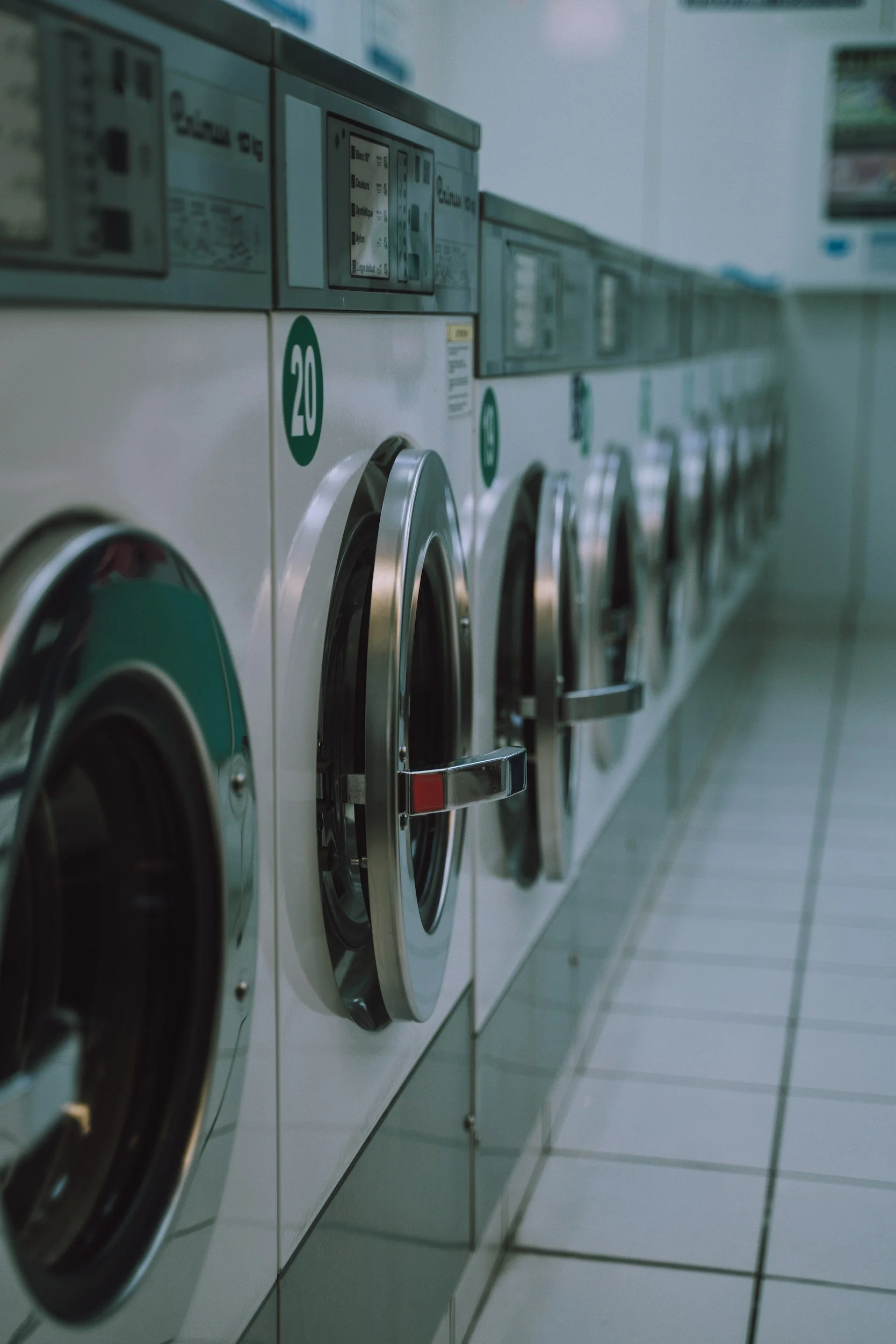 Row of coin-operated washing machines in a laundromat with tiled floor.