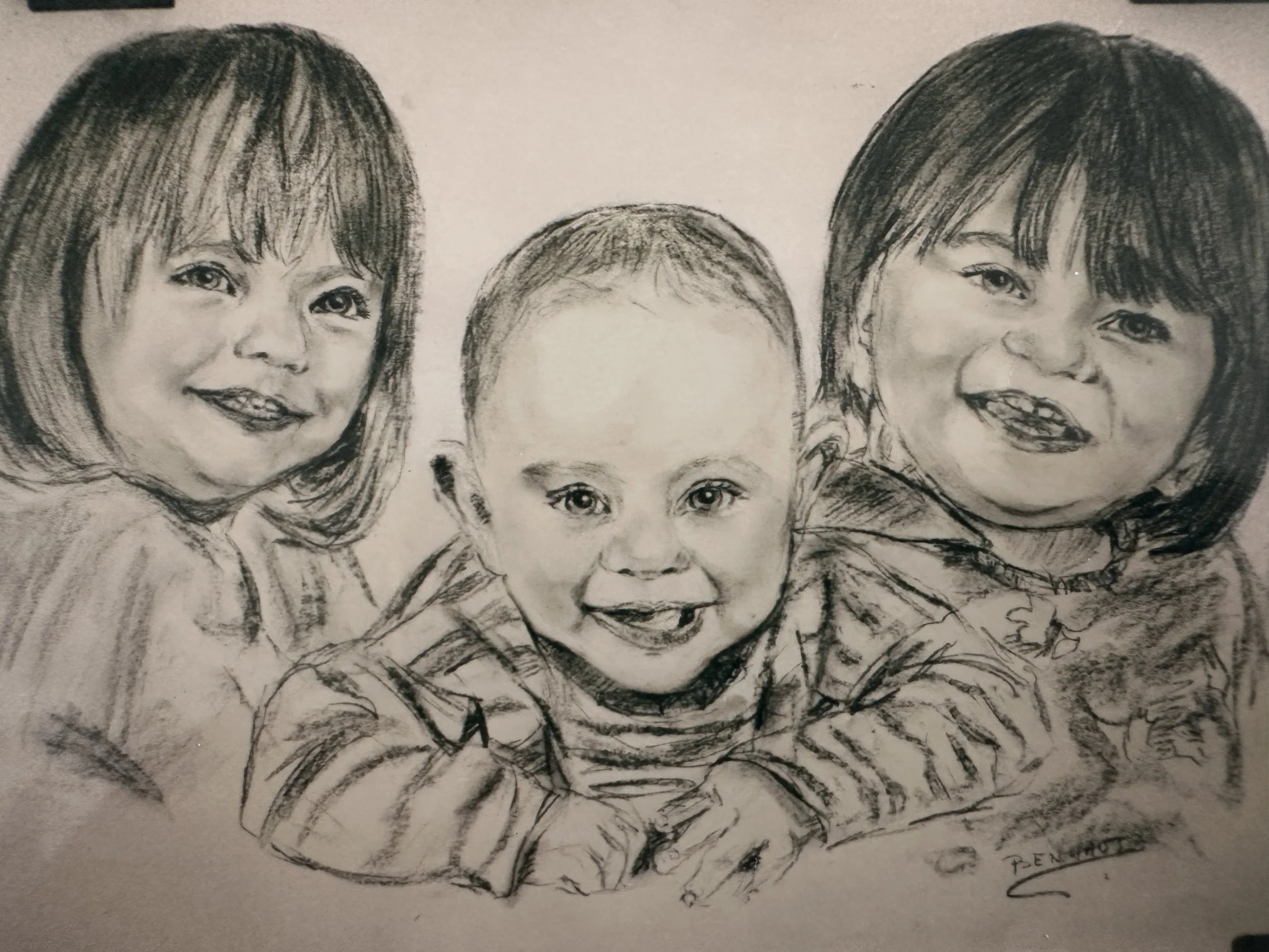 A black and white pencil sketch of three smiling children, with two girls on the sides and a boy in the middle, drawn with detailed facial features and hairstyles.