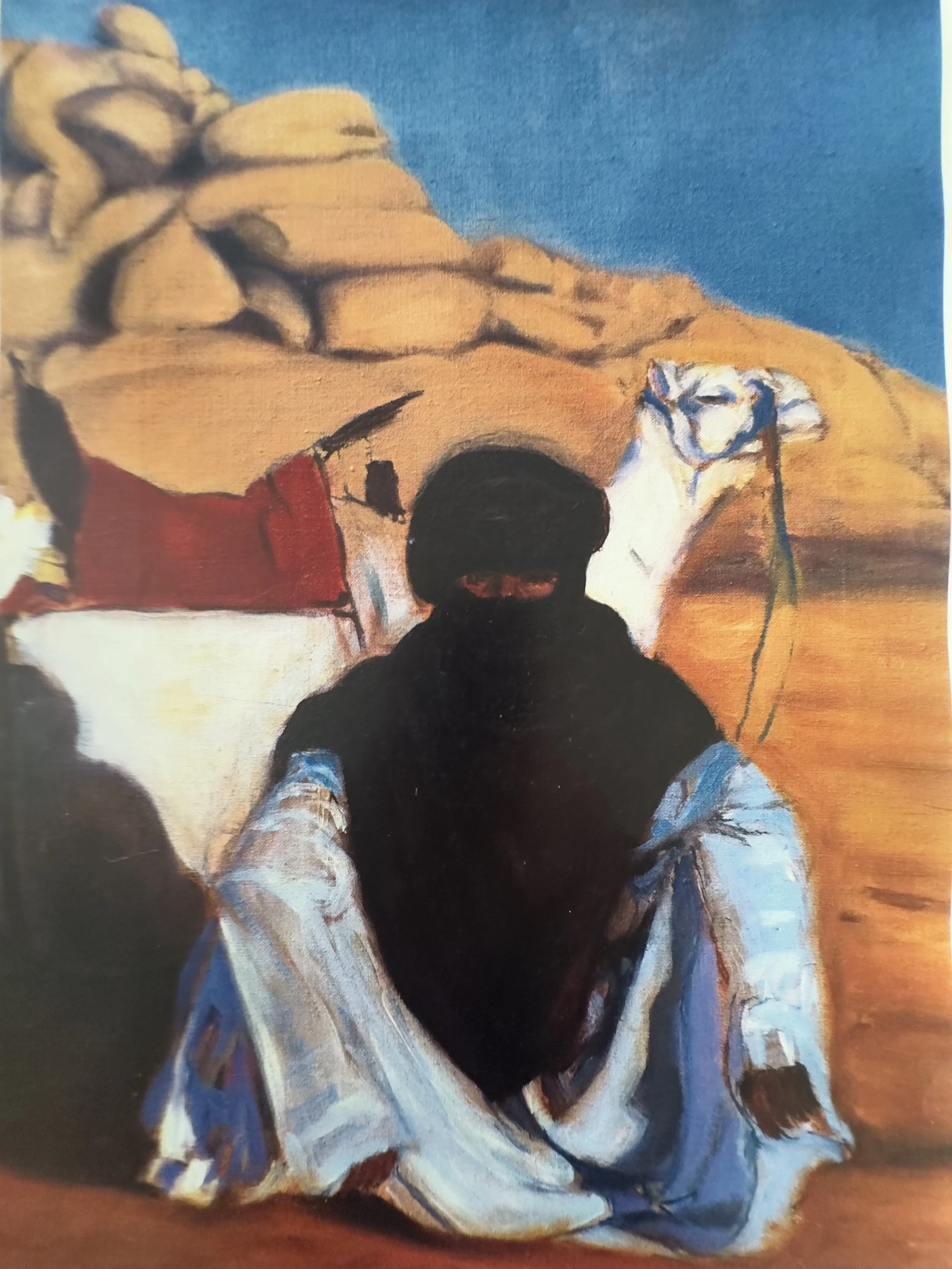 A person with dark hair wearing a light-colored shirt, seated or kneeling, with a bright blue sky background and desert rock formations.
