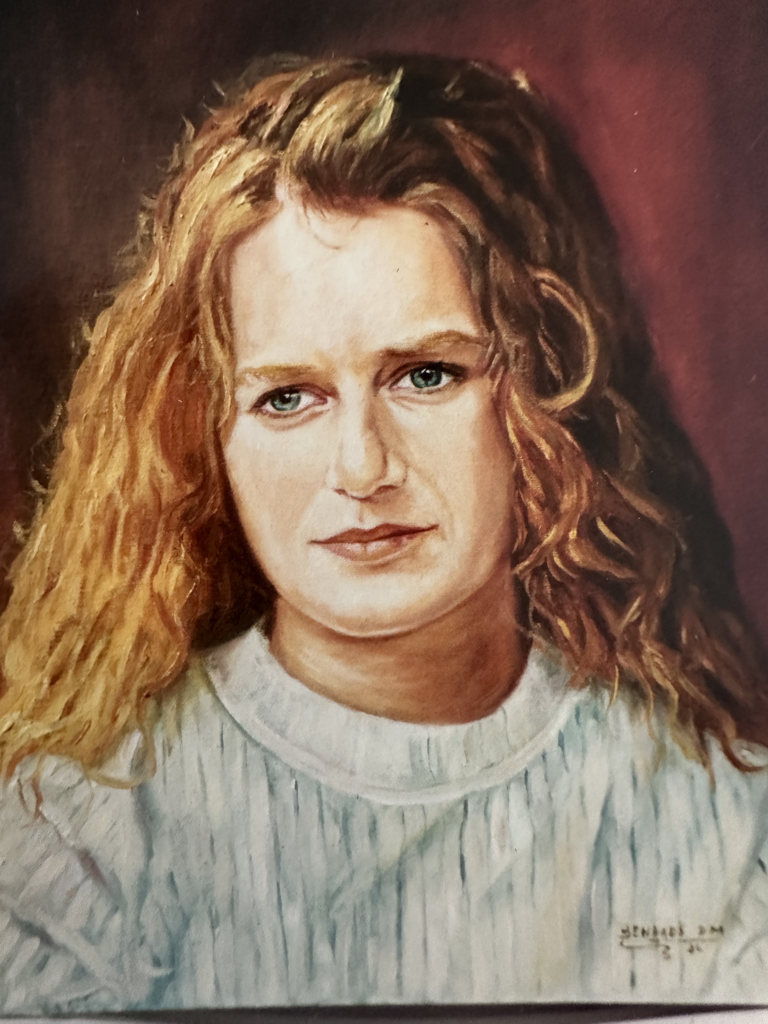 A portrait of a woman with blue eyes and wavy red hair wearing a light-colored top.