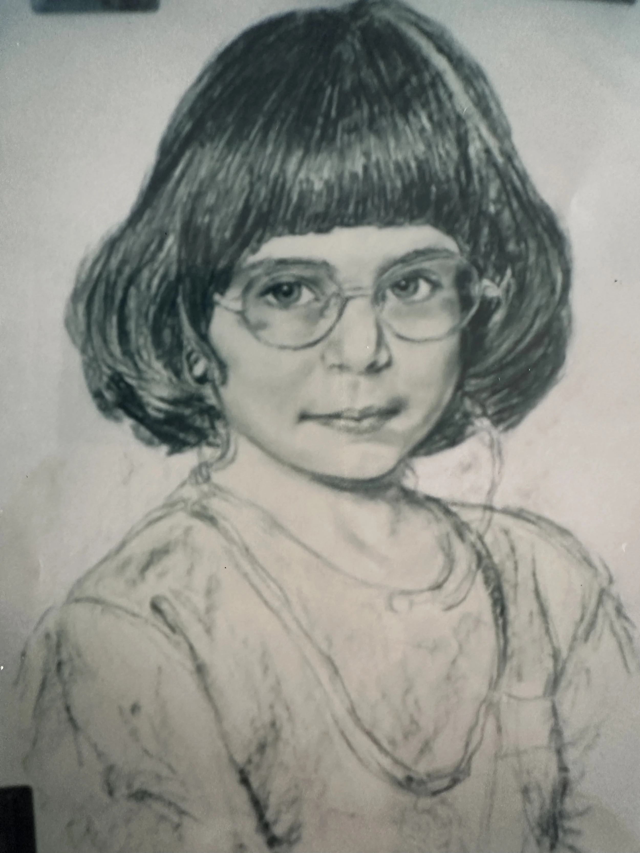 A pencil sketch of a woman with short, dark hair, wearing glasses, and a top with a rounded collar.