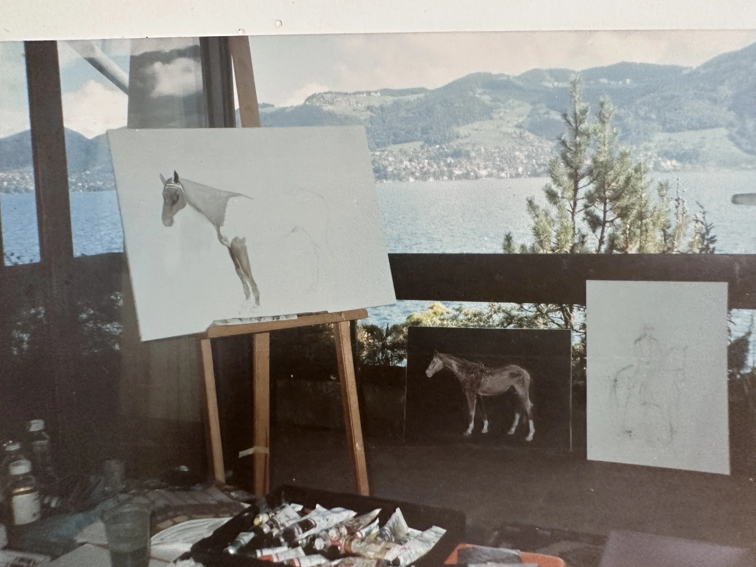 Painting of a white horse on an easel in front of a landscape with mountains and trees