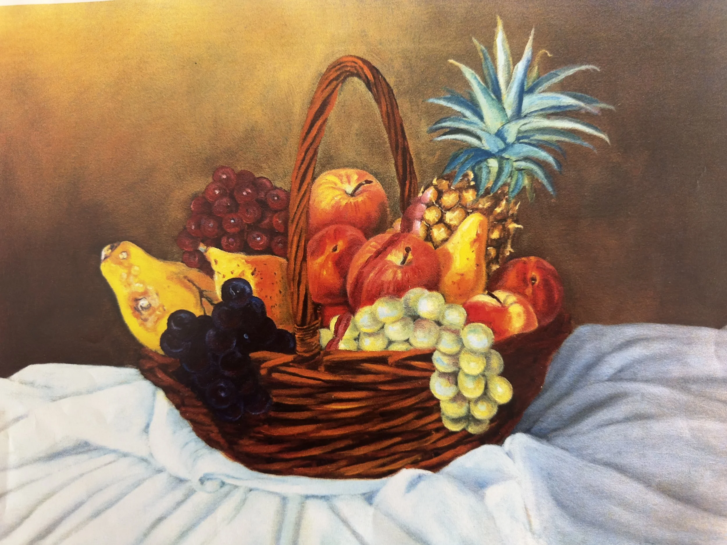 A basket of assorted fresh fruits, including grapes, apples, pineapple, banana, and berries, resting on a white cloth.