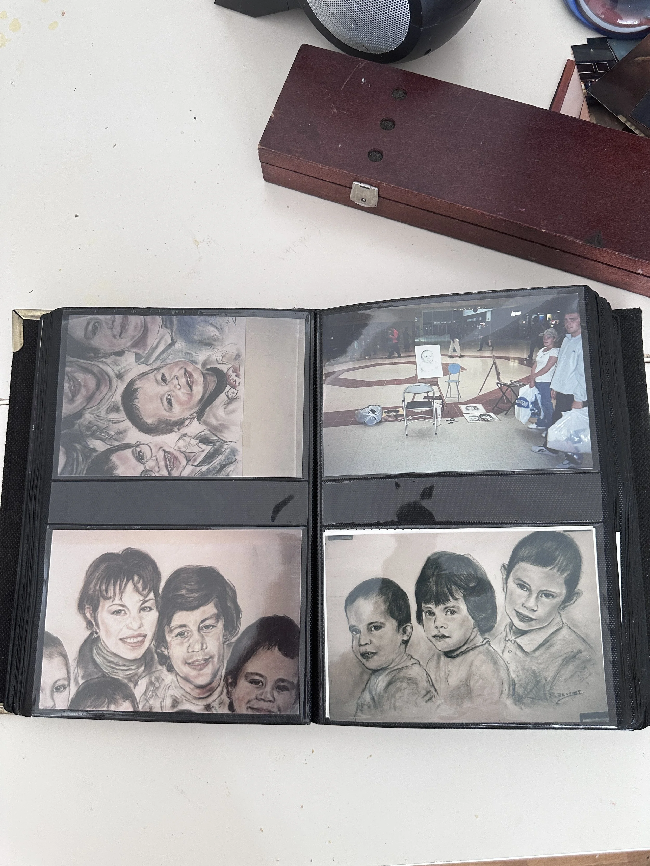 Open photo album displaying portrait sketches of children on the left page and a realistic portrait of two children on the right page.