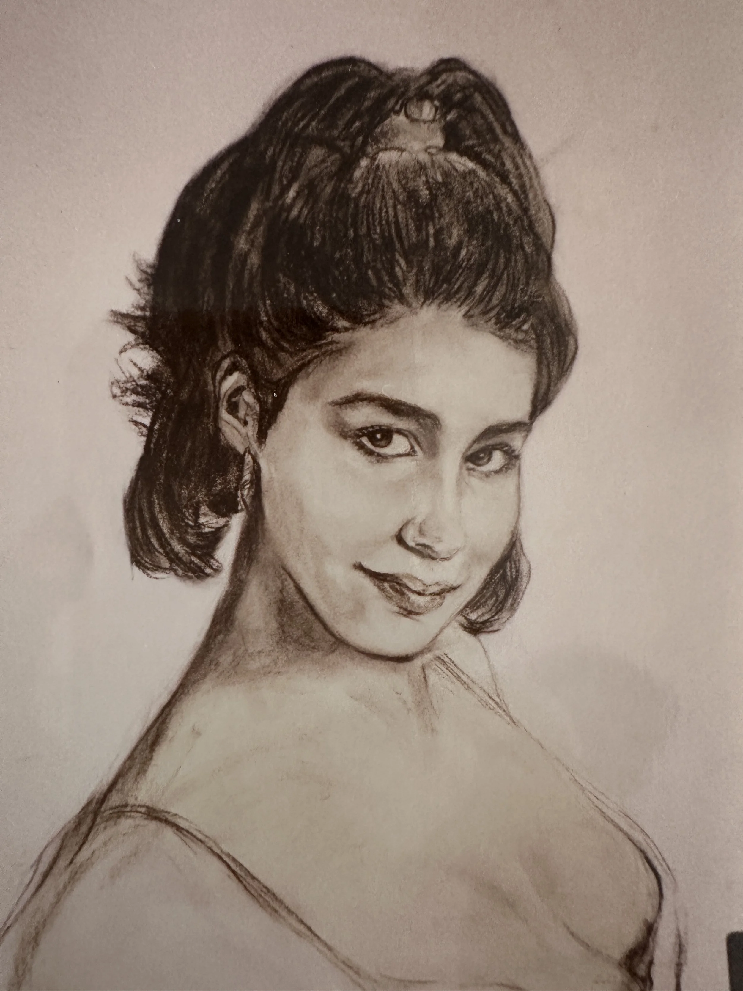 A detailed black and white pencil sketch of a woman with styled hair, expressive eyes, and a subtle smile, wearing a strapless top.