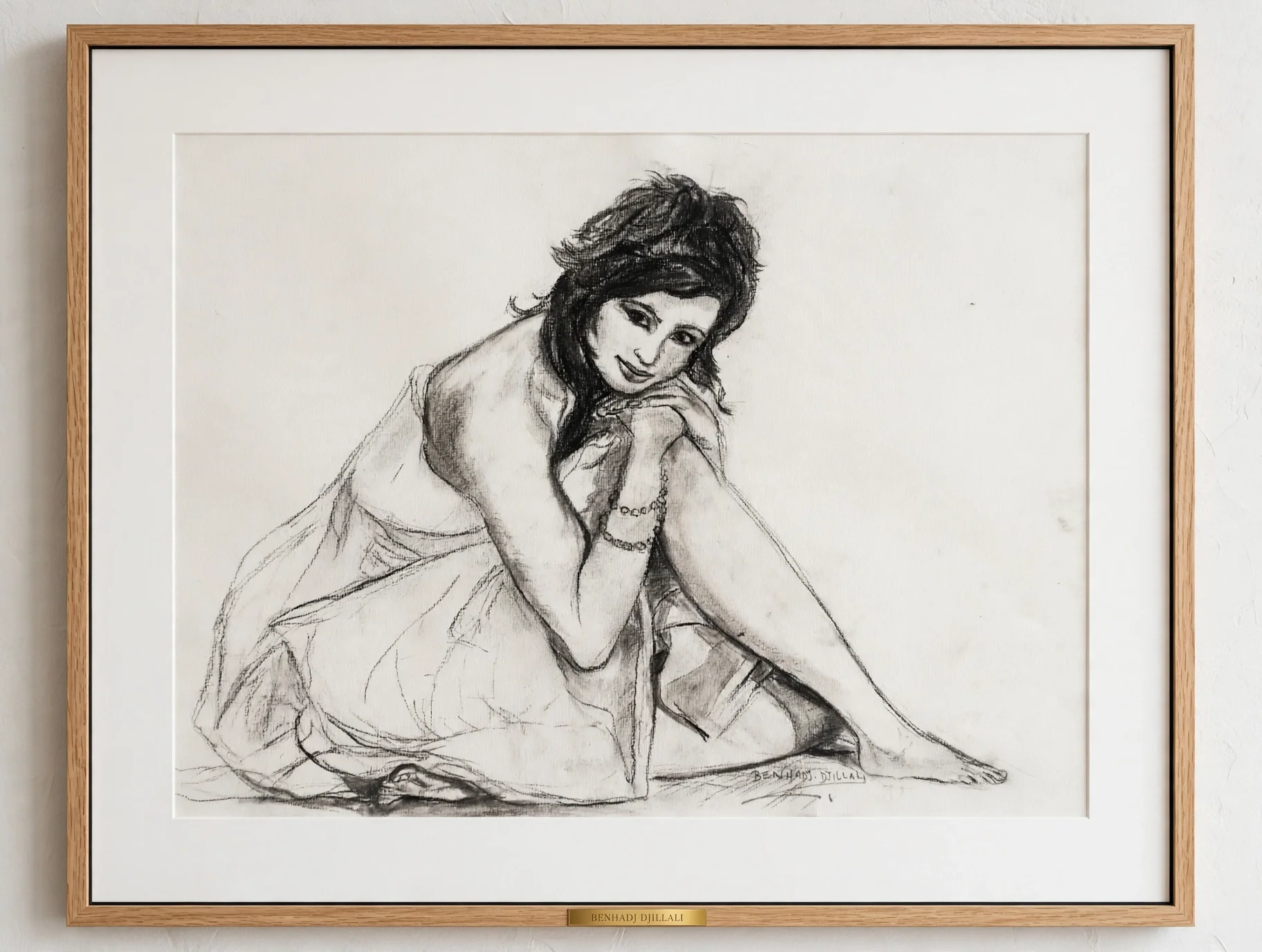 Black and white sketch of a woman sitting with her legs crossed, smiling and resting her chin on her hand. She has shoulder-length hair and is wearing bracelets. The sketch is framed and signed by Benhadi Djillali.