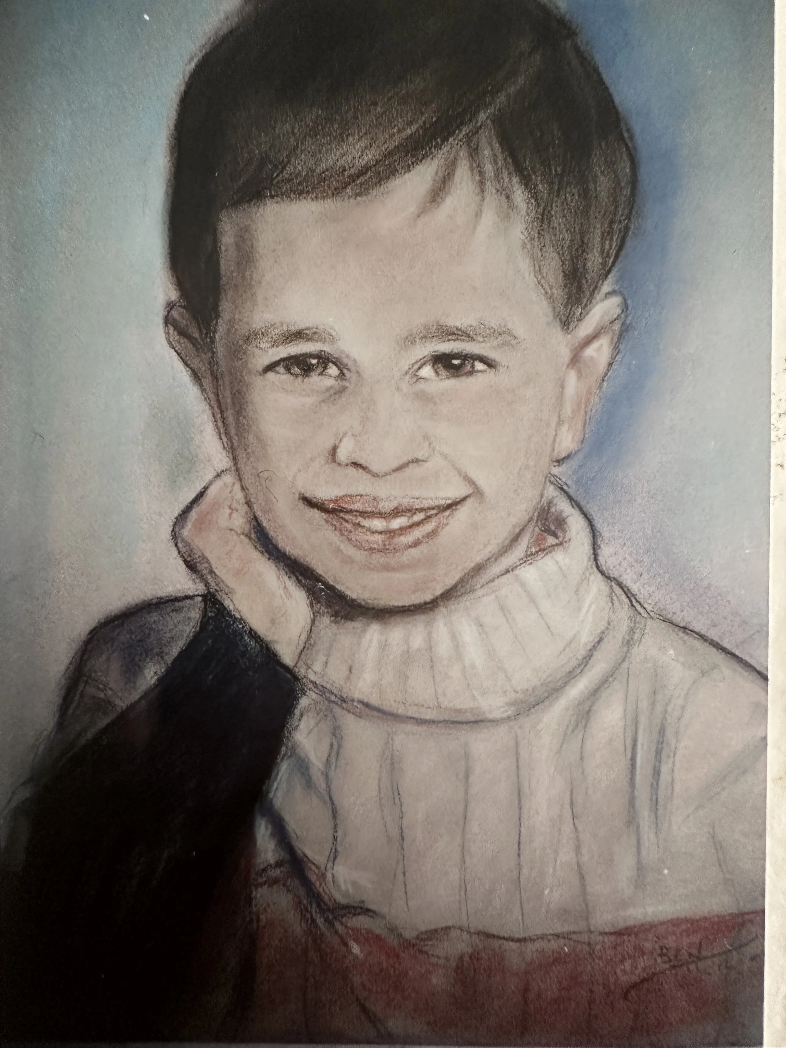 Hand-drawn portrait of a young child with short hair, smiling and wearing a turtleneck sweater, with a shadow from a hand partially covering the lower part of the drawing.