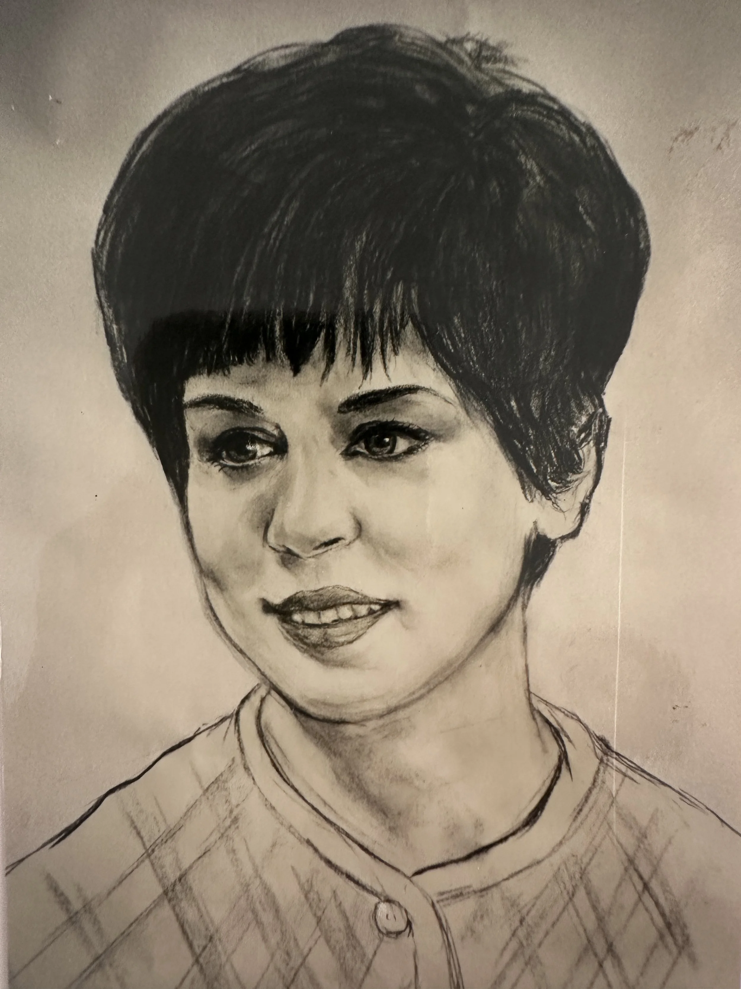 Hand-drawn pencil sketch of a woman with short dark hair, expressive eyes, and a slight smile, wearing a collared shirt with a checkered pattern.