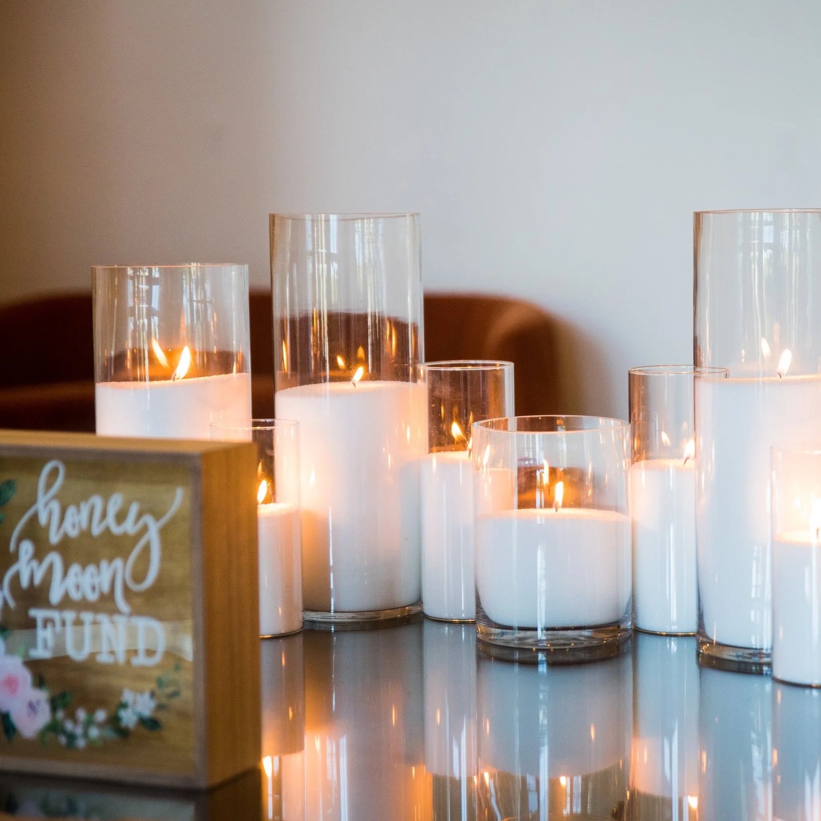 Several candles in clear glass holders of varying heights, lit and creating a warm glow on a reflective surface.