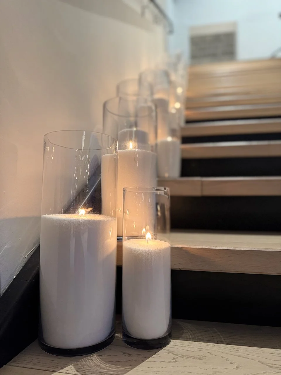 A line of cylinder vases filled with pearled wax glowing along a wooden staircase