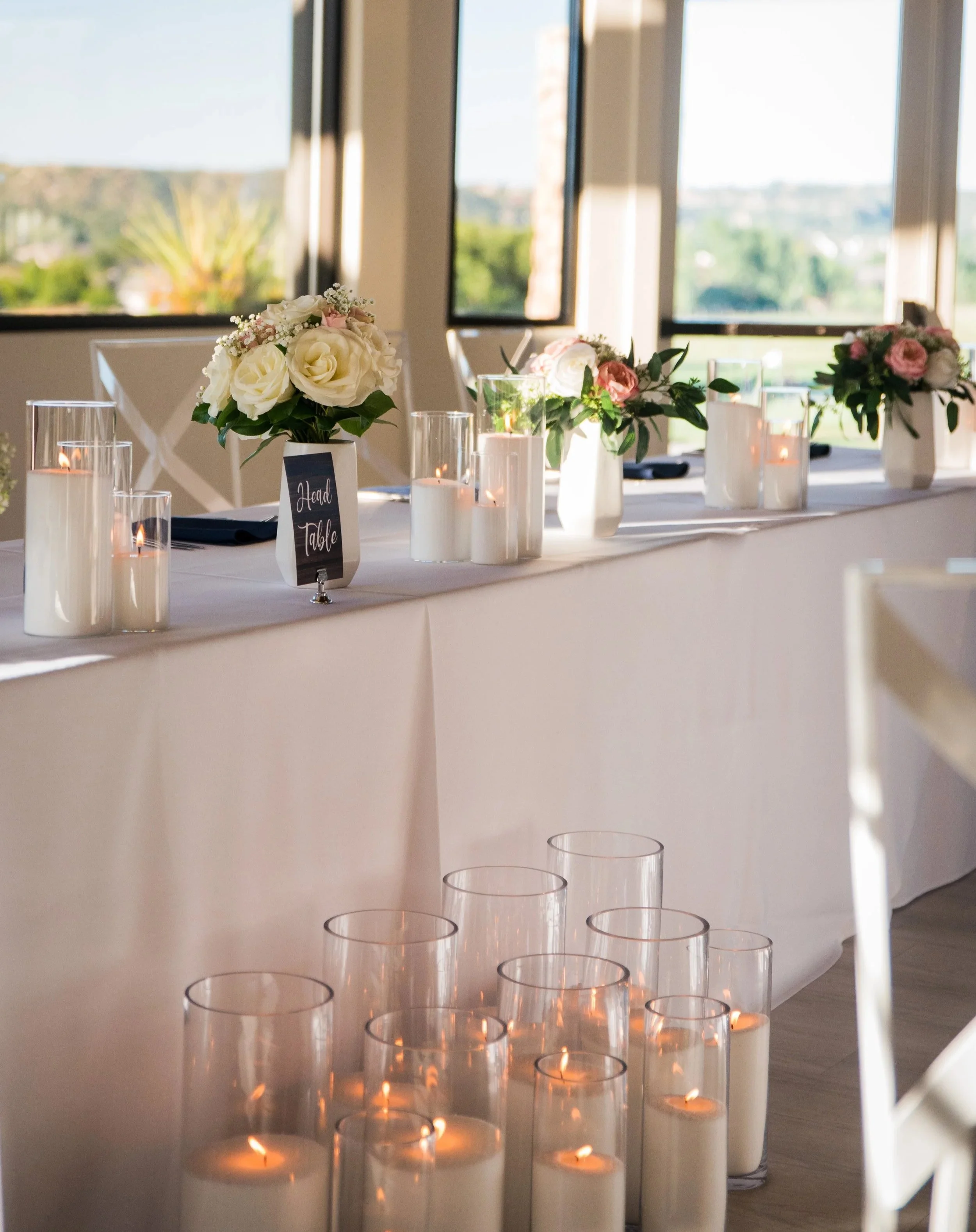 A head table at a wedding decorated with white sand wax candles styled by Colorado Candle Studio