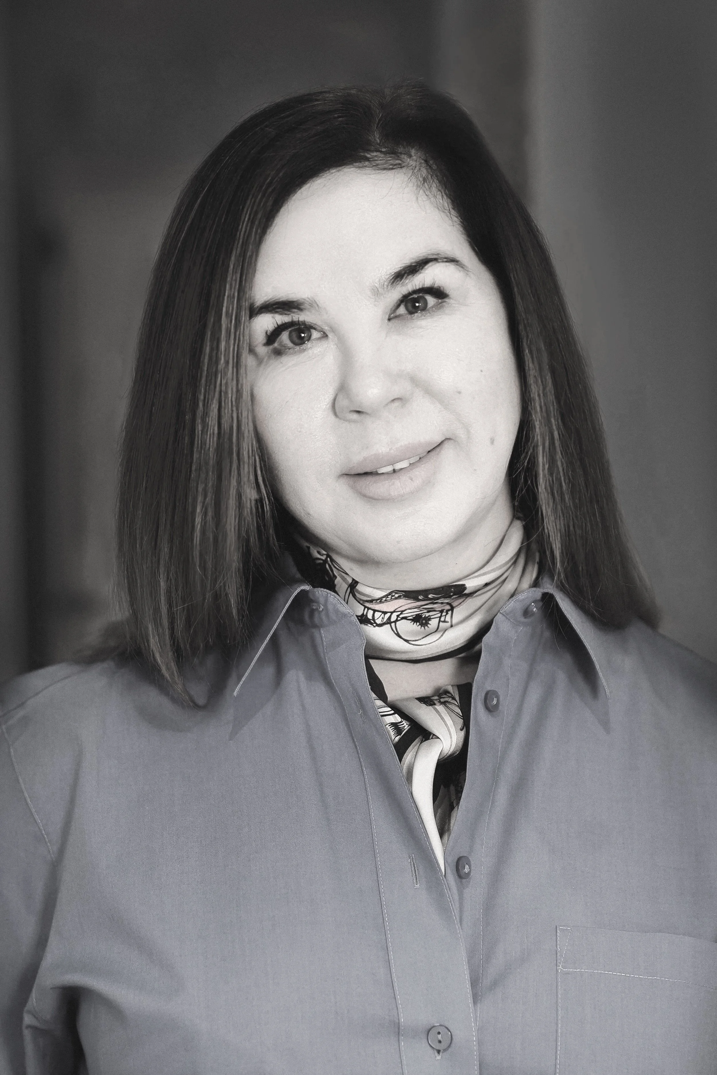 Black and white photograph of Victoria Zames with dark, shoulder-length hair, wearing a collared shirt and a scarf around her neck, smiling slightly.