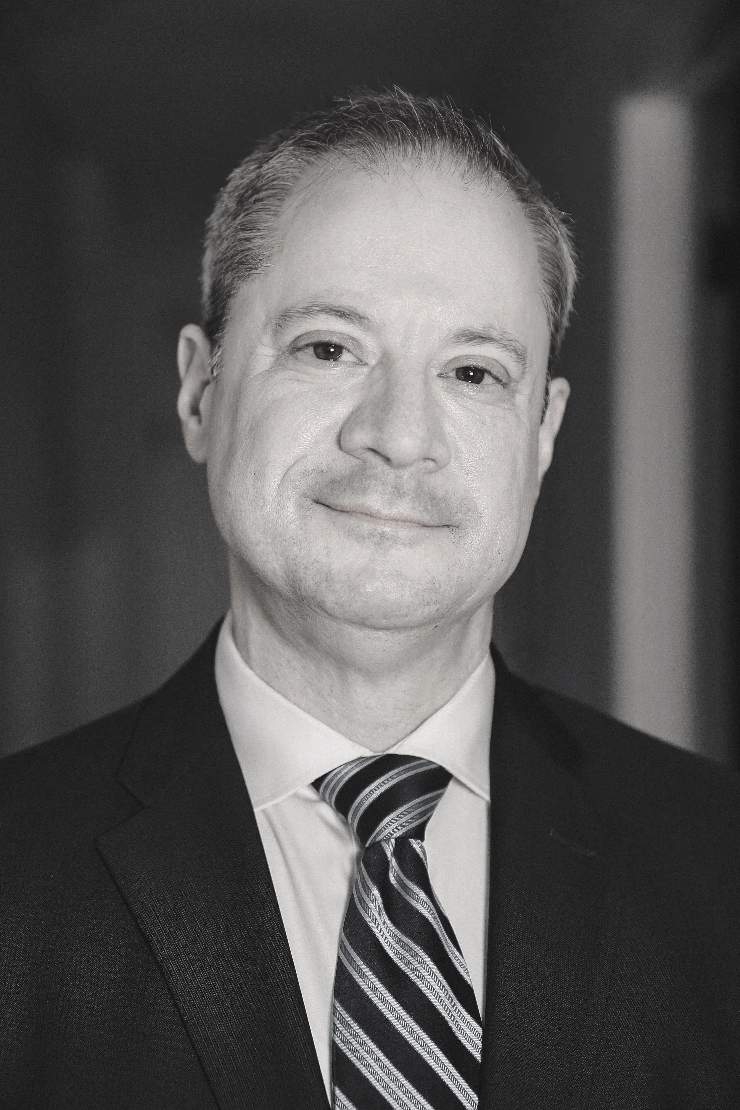 Black and white portrait of Dr. William Berger wearing a suit, dress shirt, and striped tie, smiling slightly.