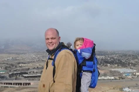 Joe McCloskey hiking in Colorado with family, carrying a child in a backpack carrier