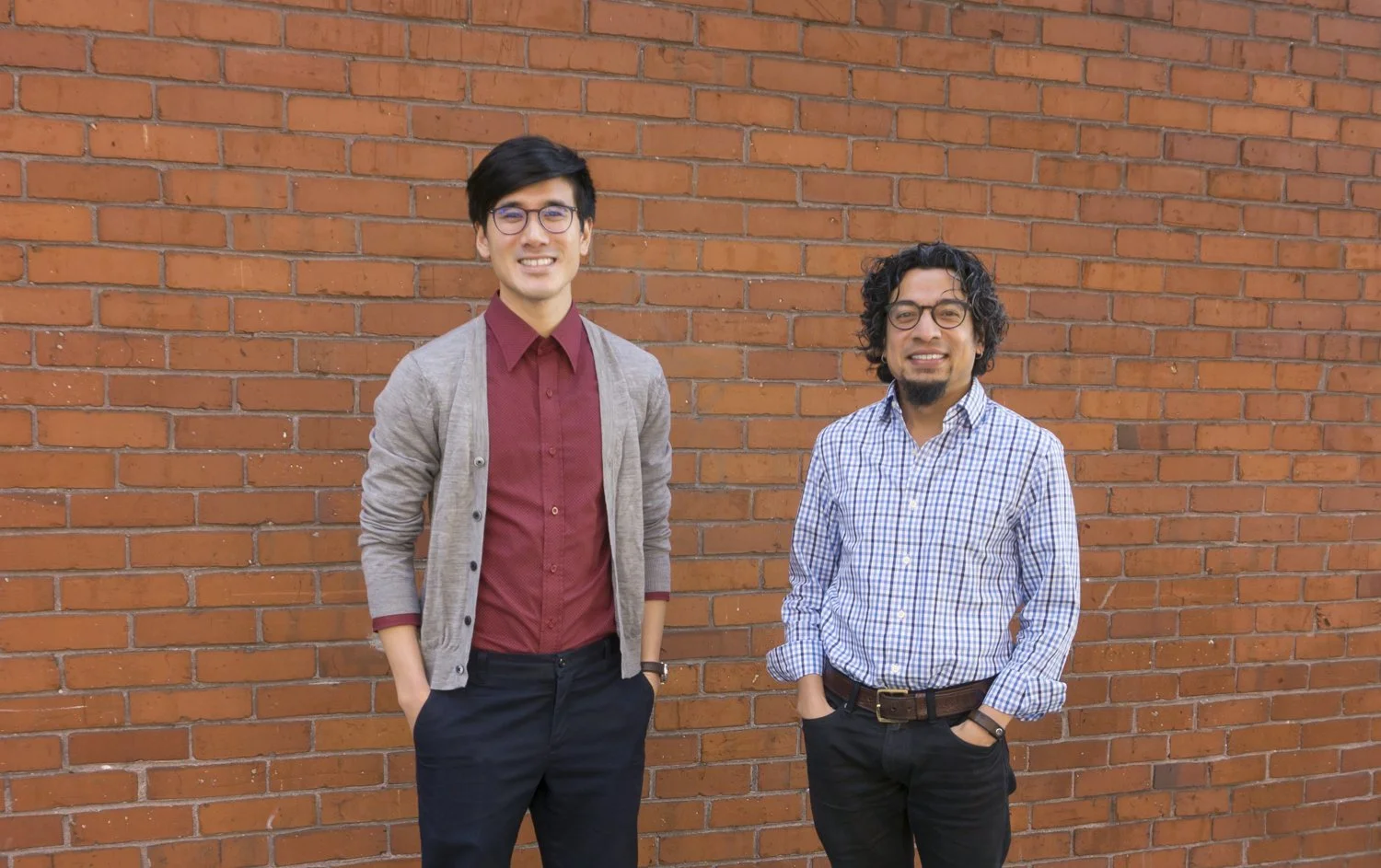 Travis and Gauri posing in front of a brick wall.