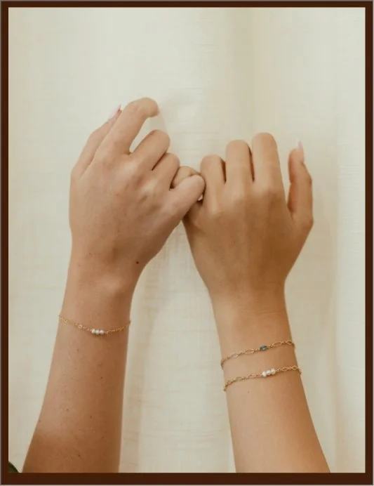 A person flipping through the pages of a notebook or journal with their hands, wearing multiple delicate bracelets on both wrists.