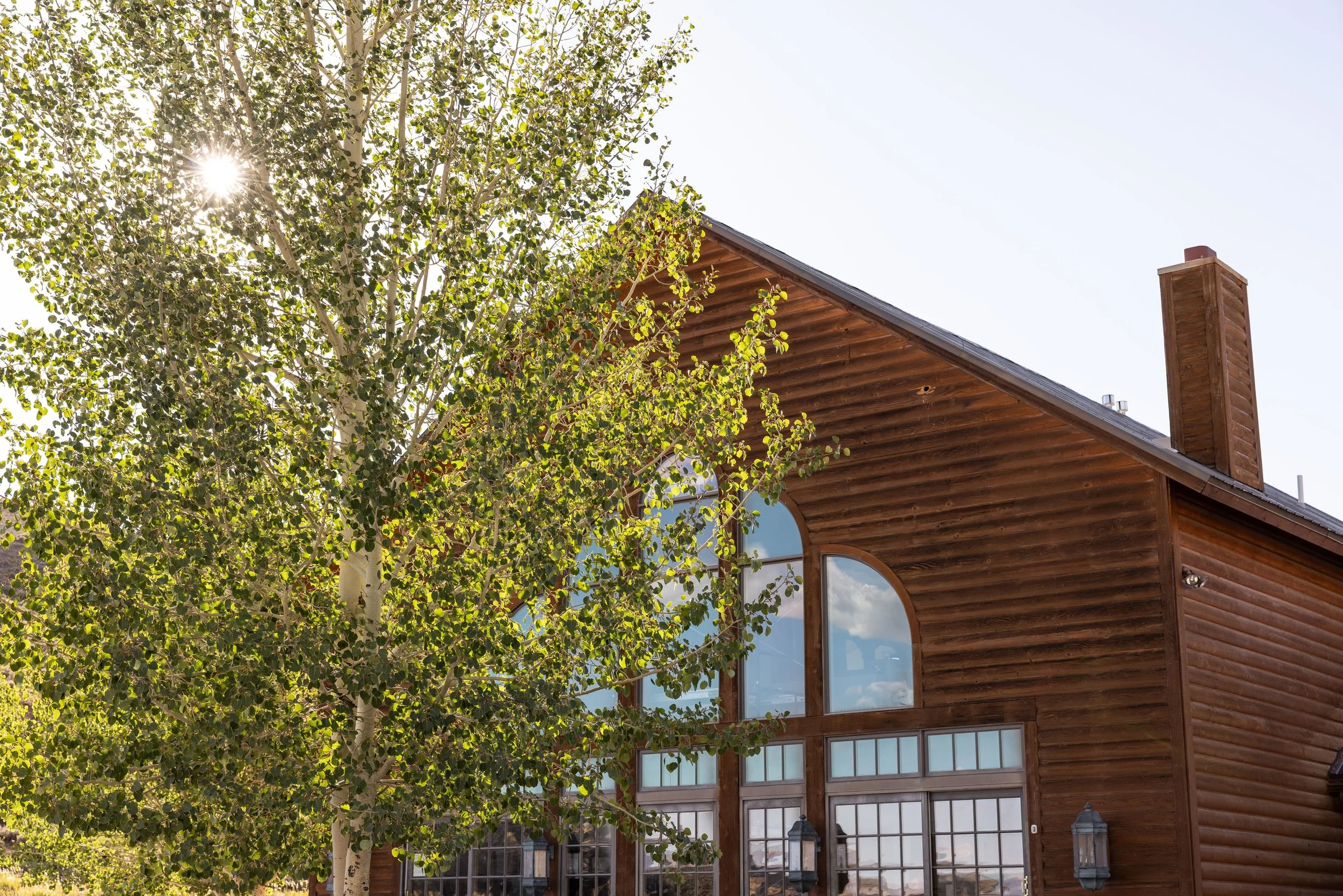 Luxury lodge and cabin rentals in Dubois, Wyoming. Dubois wedding and event venue rental. A wooden porch with two chairs, overlooking a landscape of trees and hills, with a clear sky.