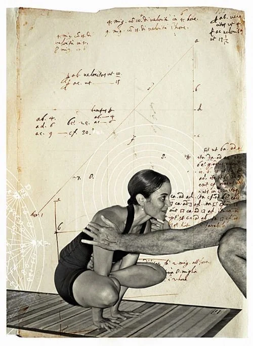 A woman practicing yoga in a squat pose with arms stretched out, touching a man's arms, in front of a wall covered with handwritten notes, diagrams, and sketches. The scene appears to be set on a wooden floor.