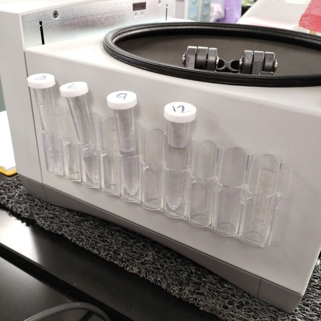 Laboratory centrifuge with sample test tubes in slots, labeled 3, 4, 5, 9, and 12.