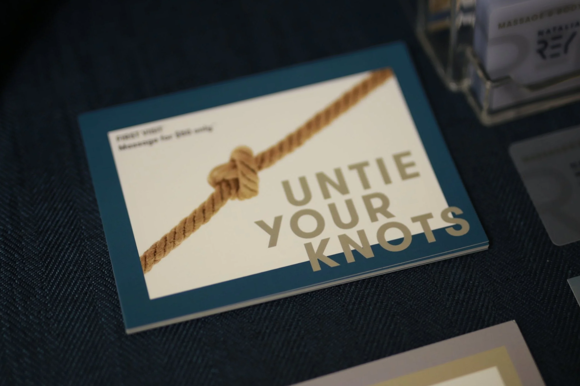 Close-up of a book titled 'Untie Your Knots' with a rope illustration on the cover, placed on a dark textured surface near a metal storage rack with boxes.