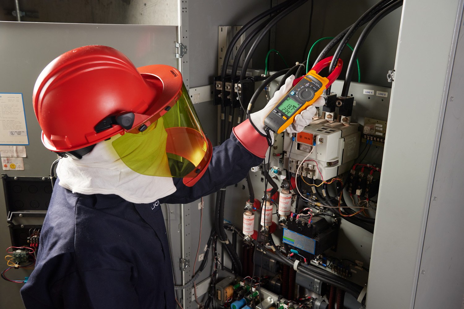 Electrical worker verifying absence of voltage while wearing arc-rated PPE and using a test instrument.