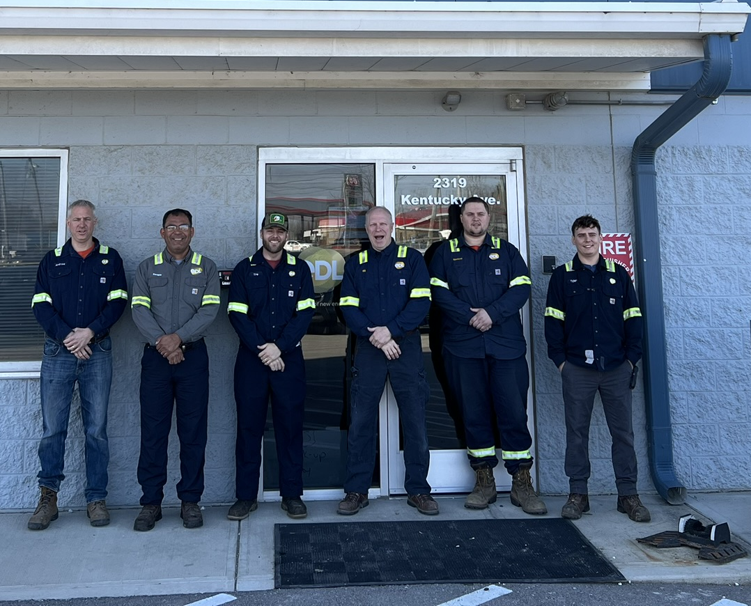 Industrial electrical crew in work uniforms outside a project office.