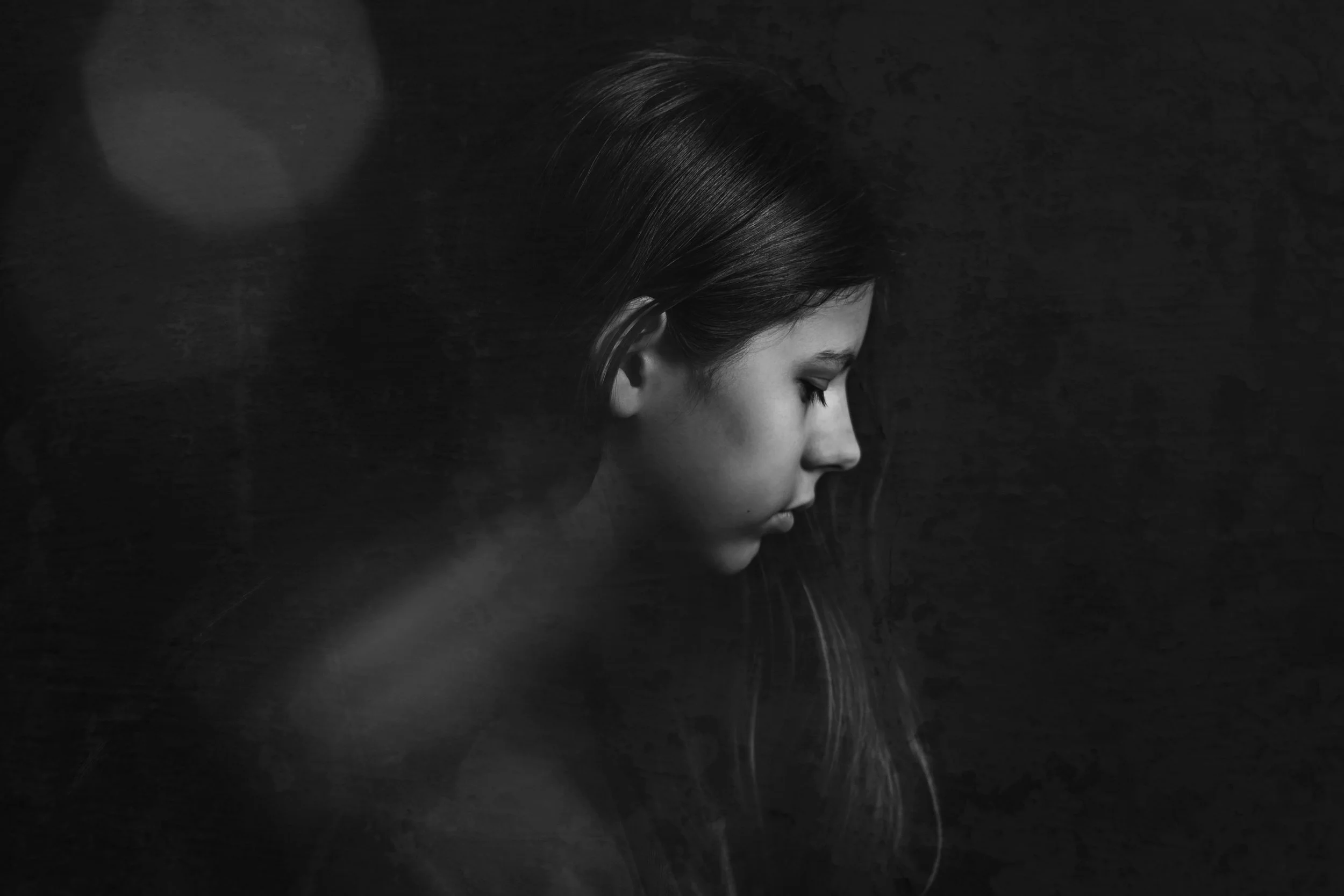 A black-and-white side profile of a woman with long hair, eyes closed, in a dark setting.