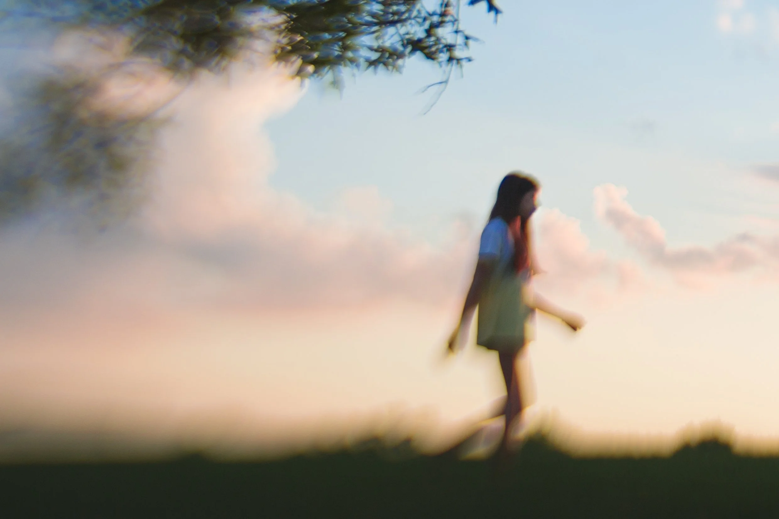 A woman walking on a hill during sunset with cloudy skies.