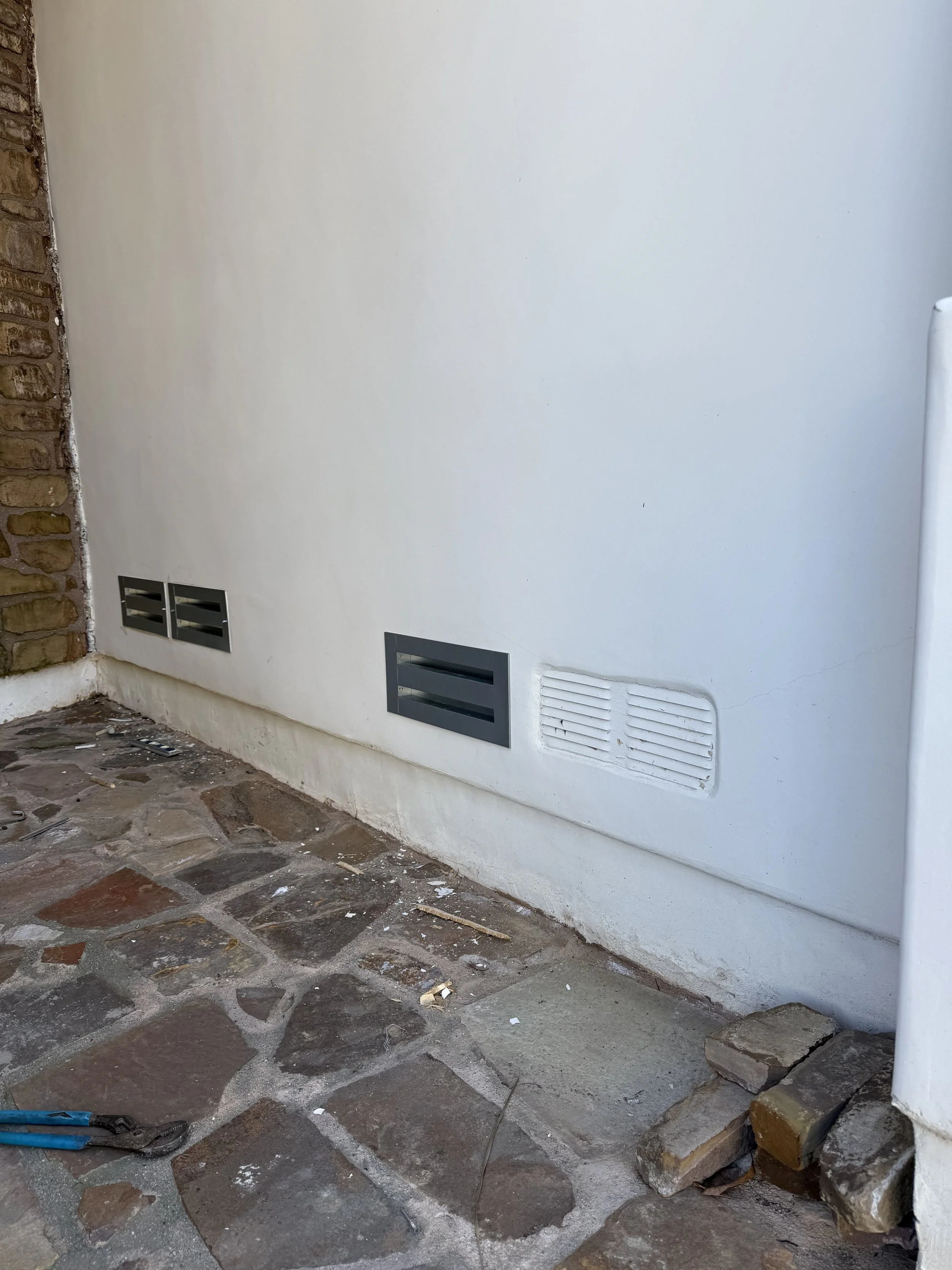 Image is a progress photo of three standard vents that have been retrofitted with BrandGuard vents ember resistant foundation vents and one vent that has not for a before and after viewpoint