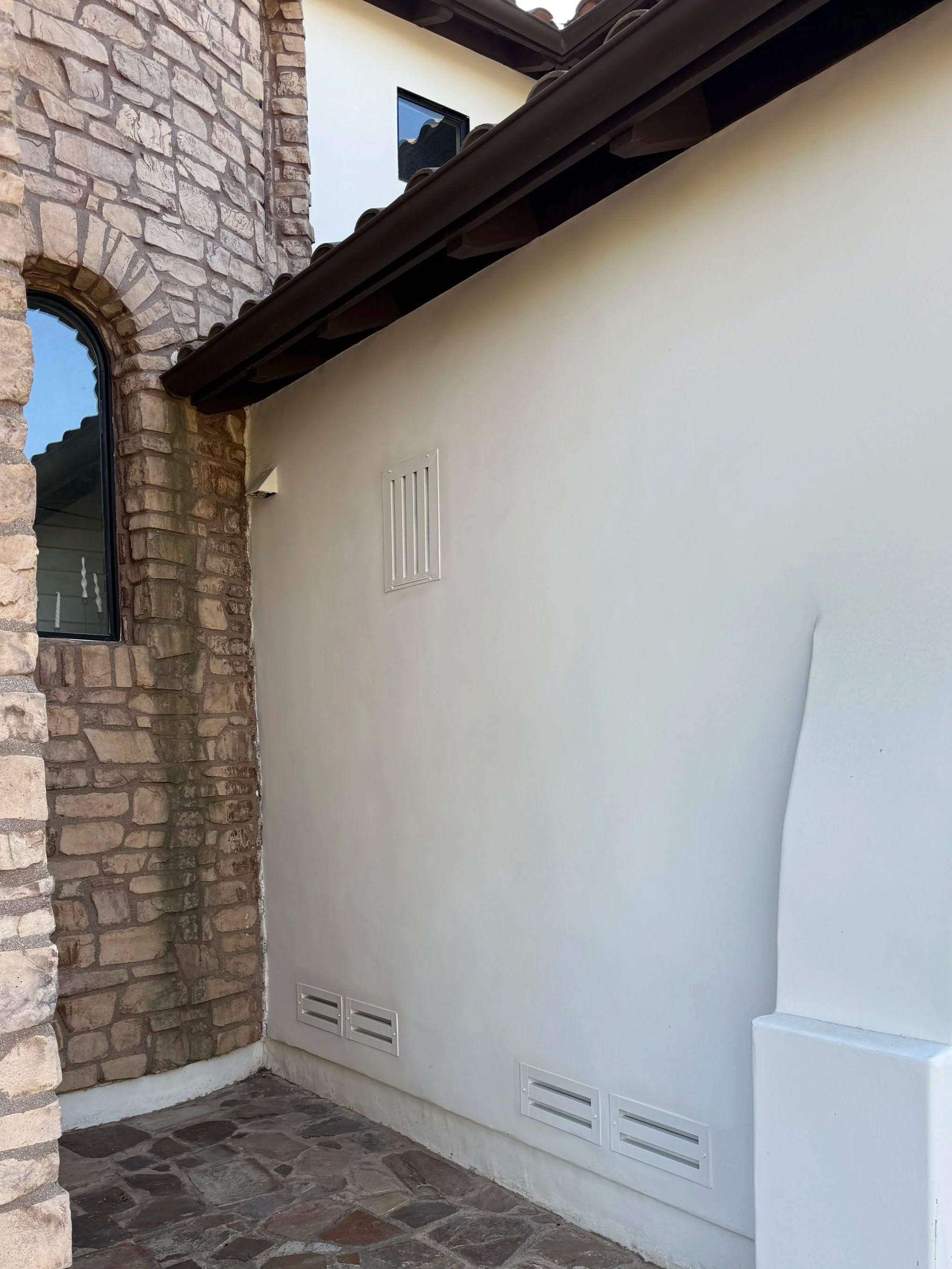 Image is of a home with stucco and stacked stone with 4 painted BrandGuard ember resistant foundation vents and 1 gable vent installed on a home