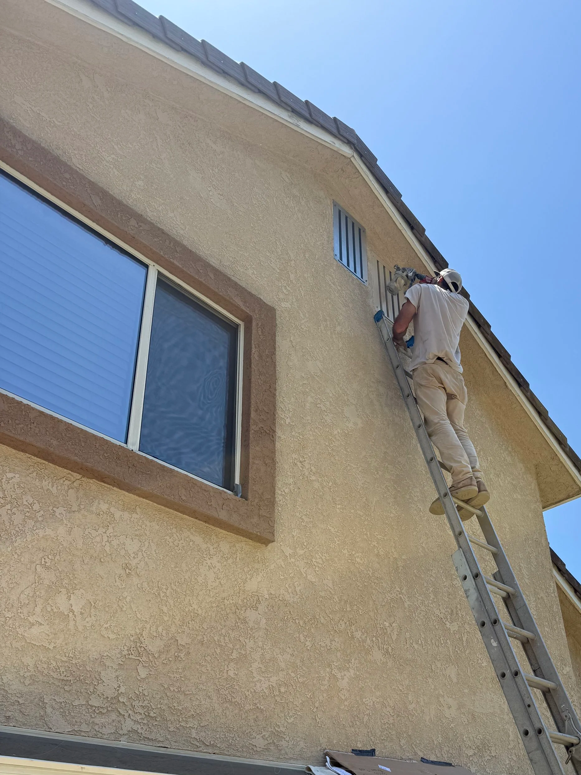 Image is of a man on a ladder spray painting a recently installed BrandGuard ember resistant gable vent