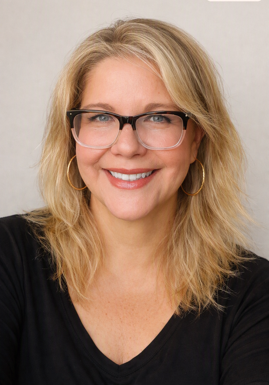 A smiling woman with blonde hair, glasses, and hoop earrings, wearing a black top.