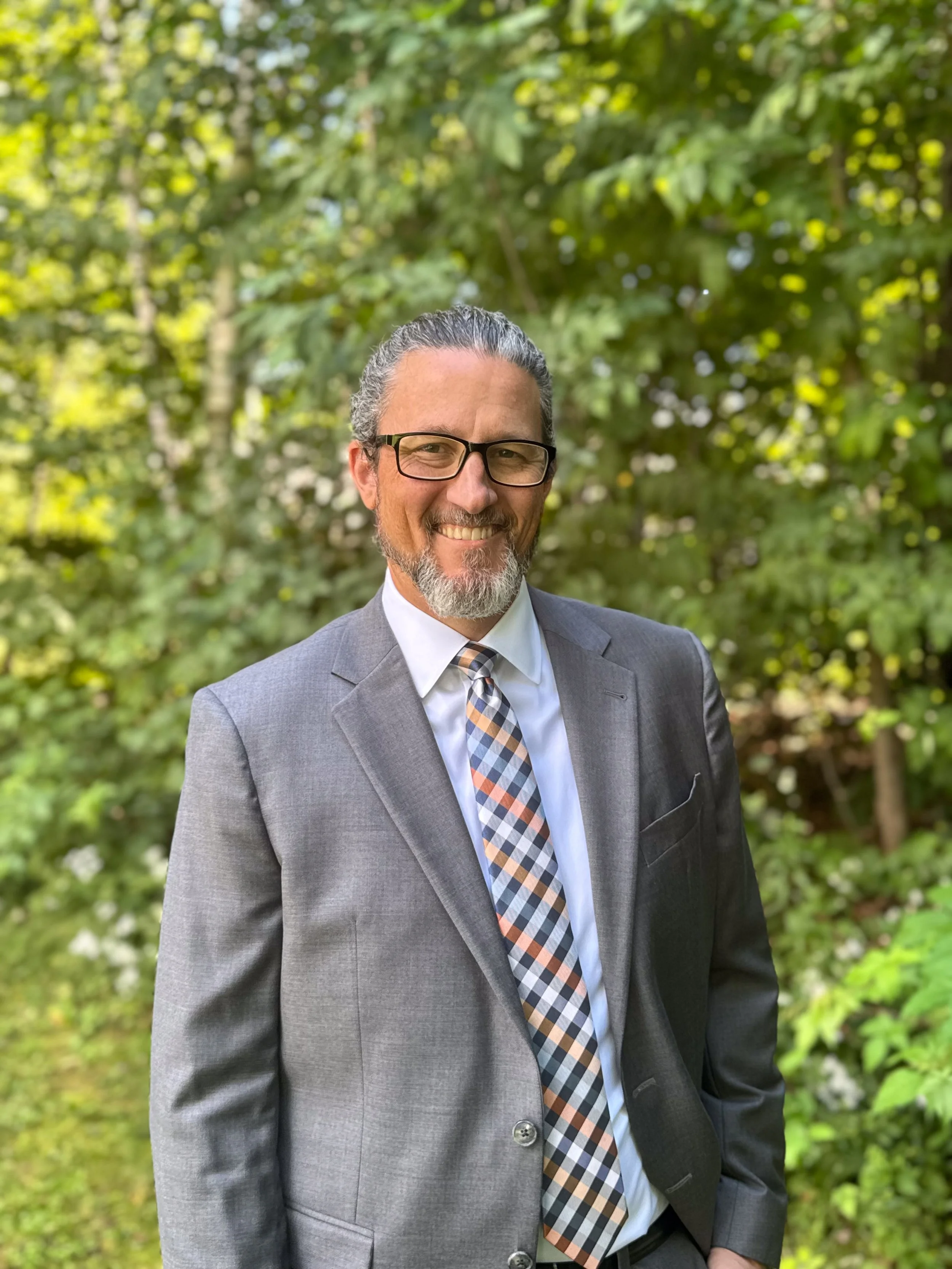 Derek Raynes in a suit and tie outdoors.