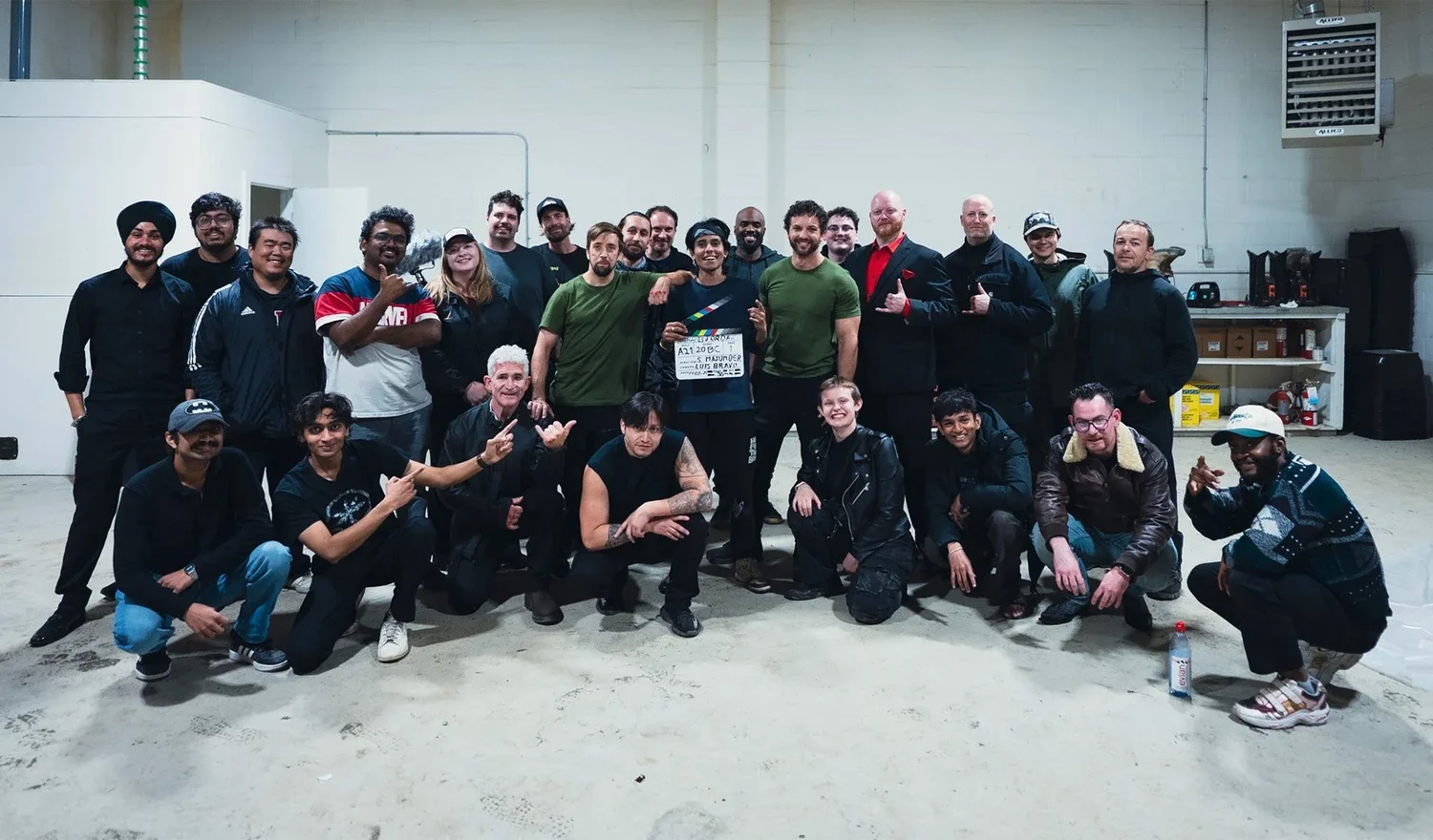 A group posing together in a production workspace, with a clapperboard at the centre.