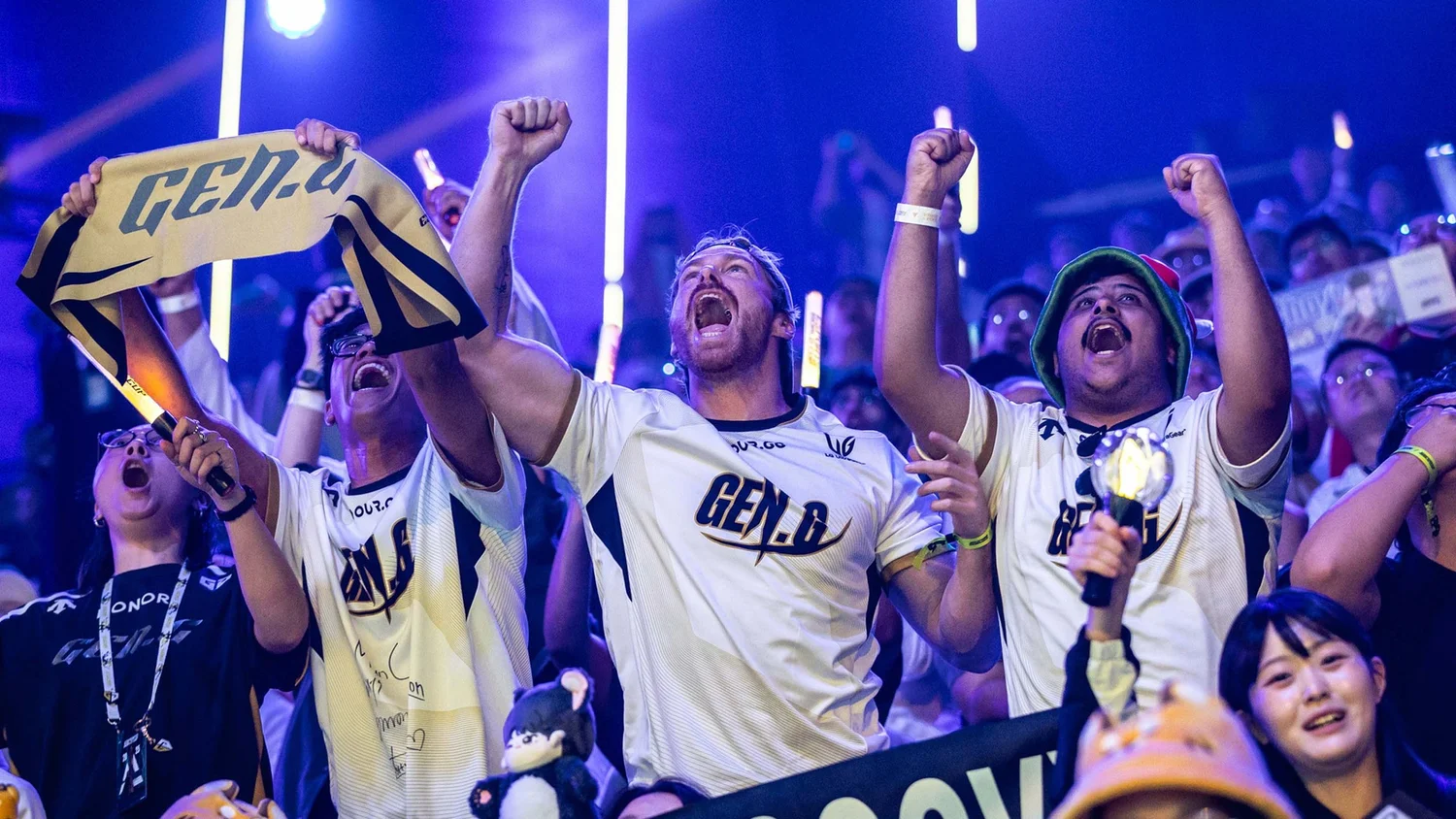 Esports fans cheering with raised arms under blue arena lighting.