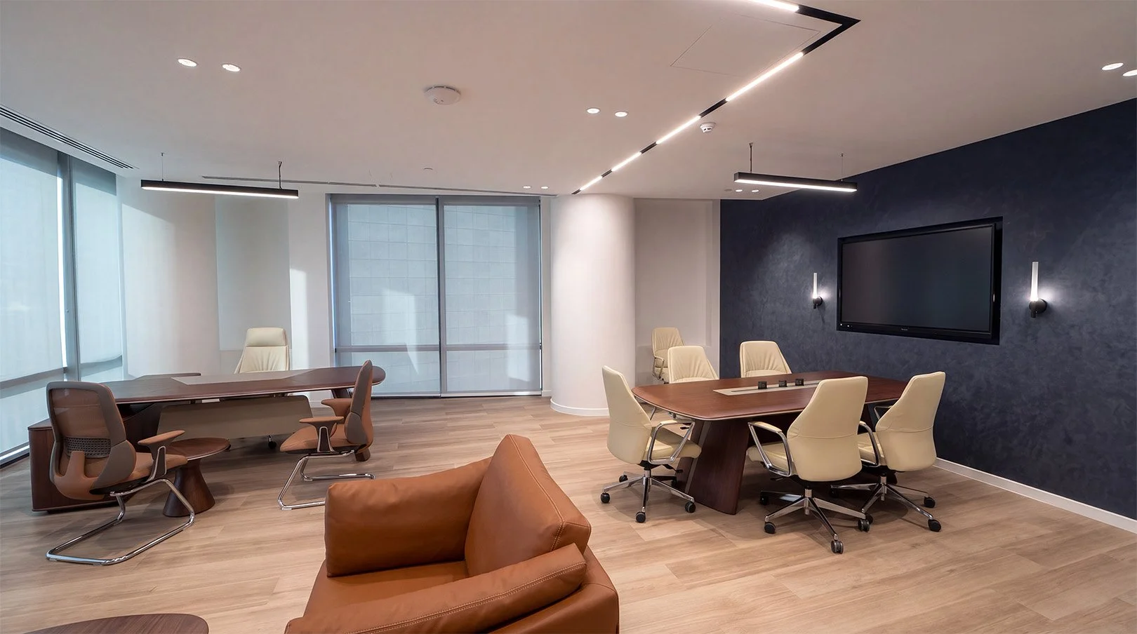Campus meeting space with tables, chairs, a wall-mounted screen and lounge seating.