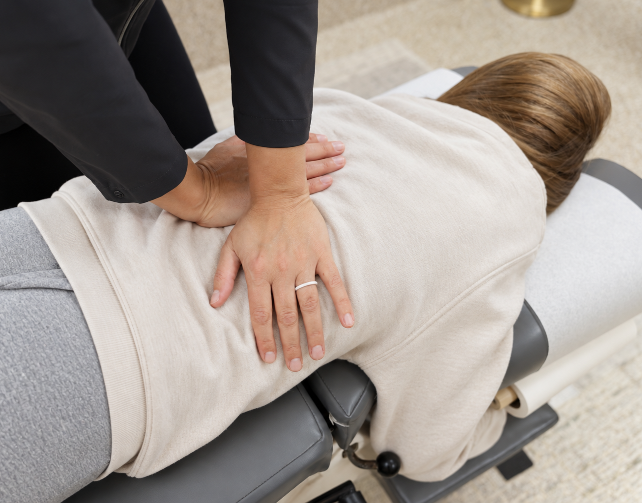 Person performing chest compressions on a patient lying face down on a massage table.