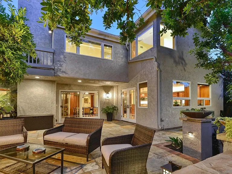 Outdoor patio area with wicker furniture, trees, and a two-story house with large windows and sliding glass doors.