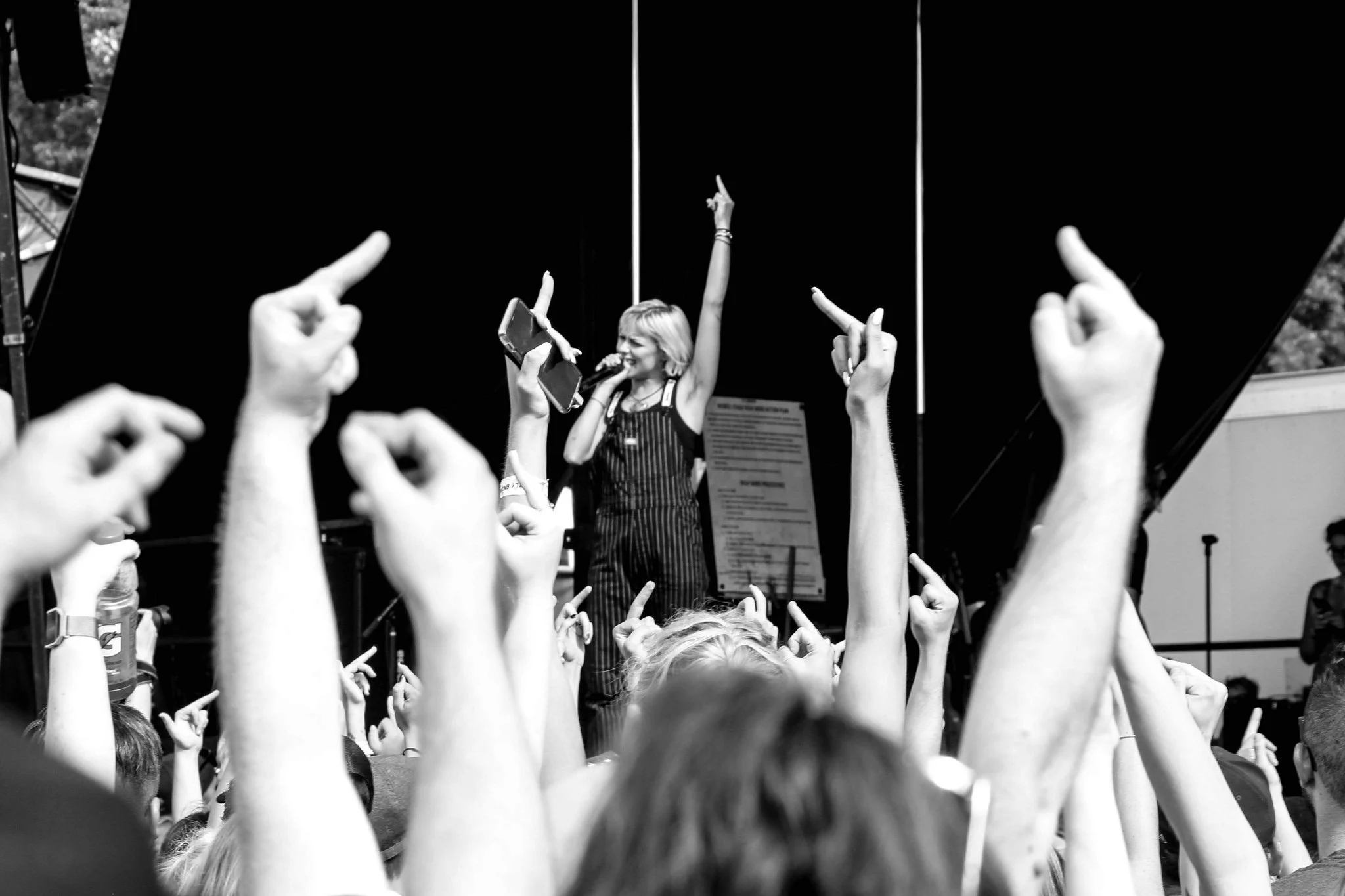 A woman with blonde hair singing on stage with her arm raised, surrounded by an audience with hands raised.