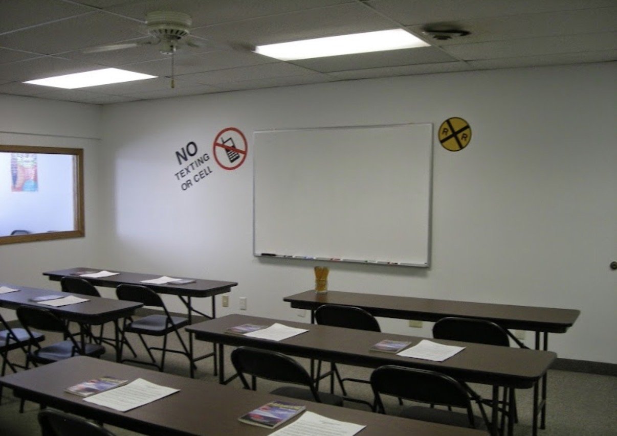 Empty classroom with tables and chairs, whiteboard on wall, no texting or cell phone sign, and radiation hazard sign.
